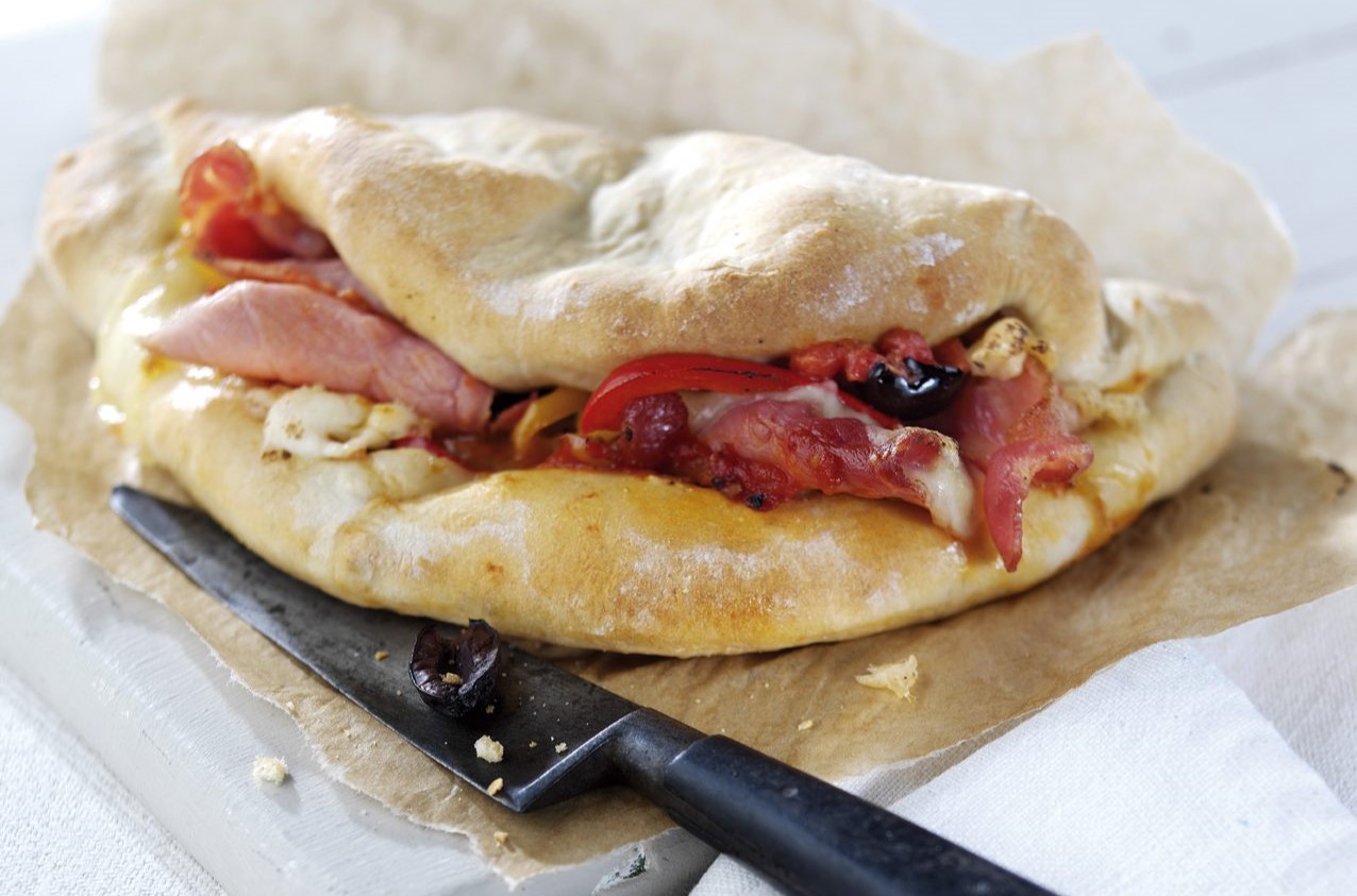 Folded bacon calzone on a wooden board with a black handled knife