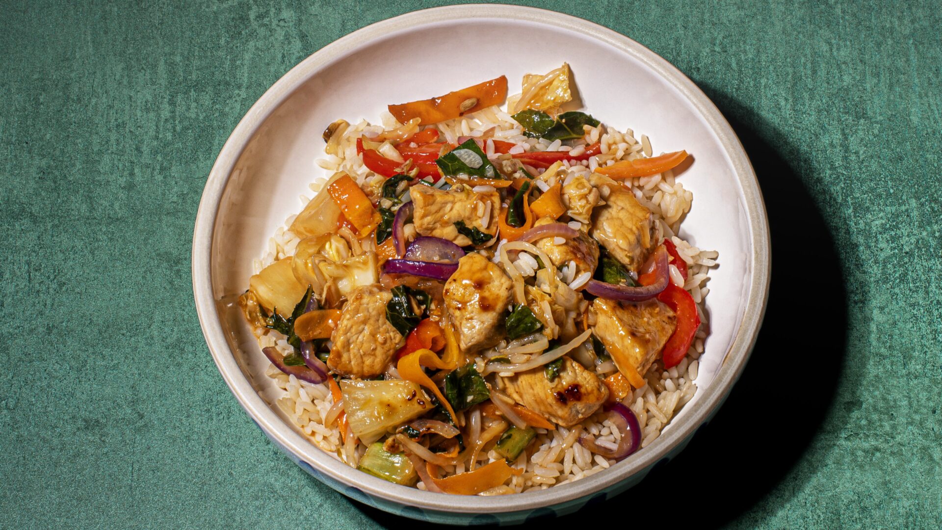 Sweet and sour pork stir-fry with brown rice served in a white bowl