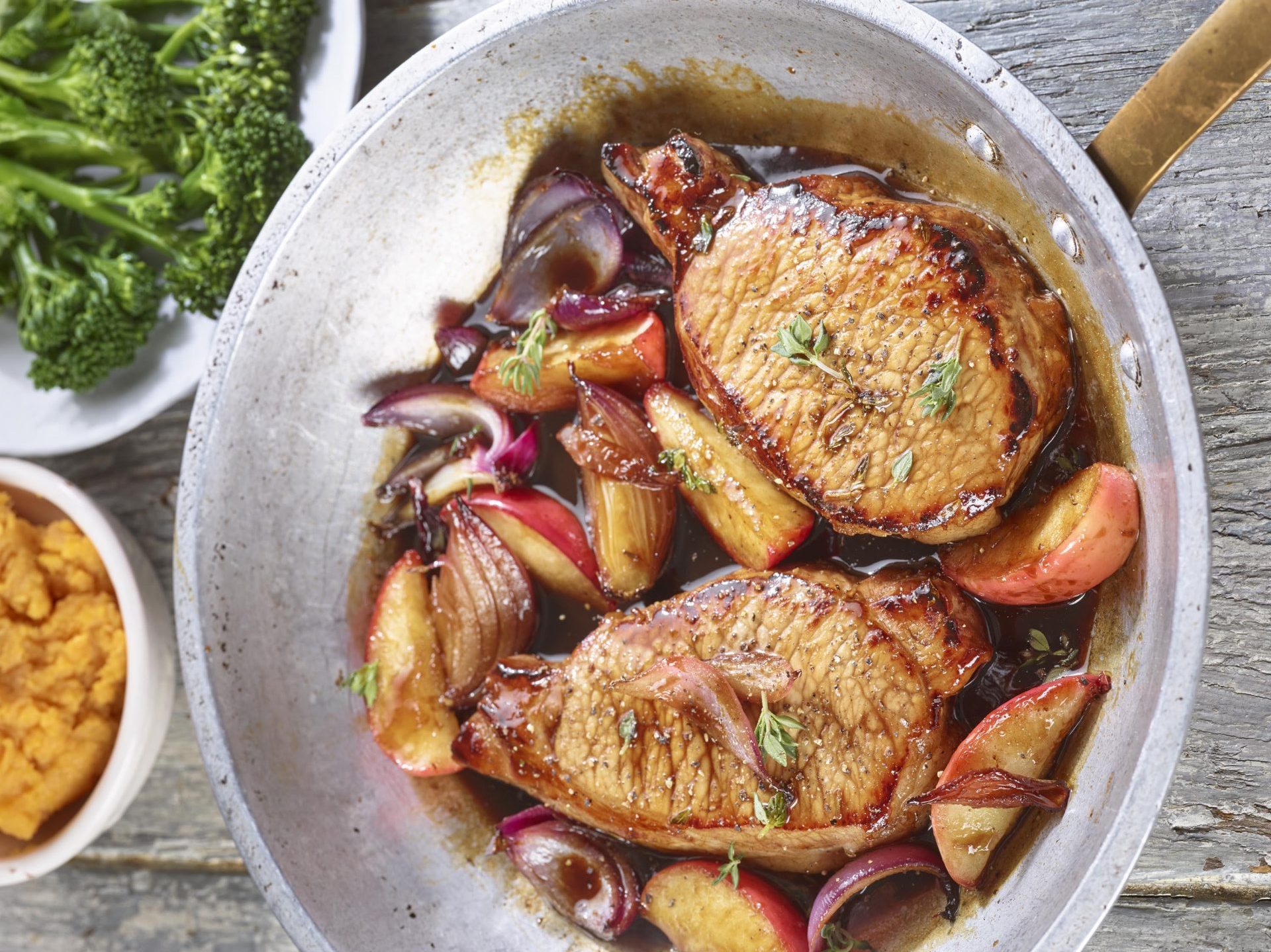 Silver frying pan containing two pork chops with apples in a balsamic sauce