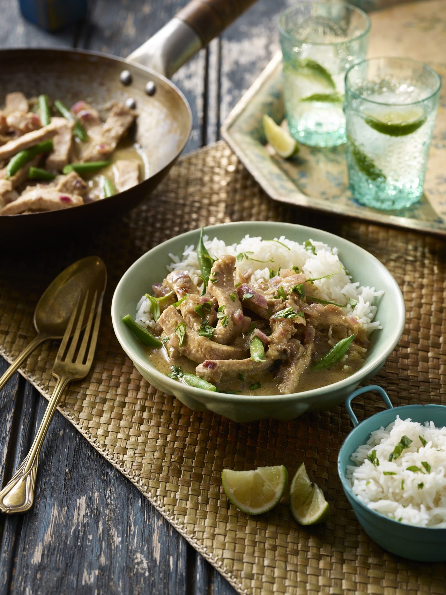 Central bowl of thai curry served with rice, with frying pan in background