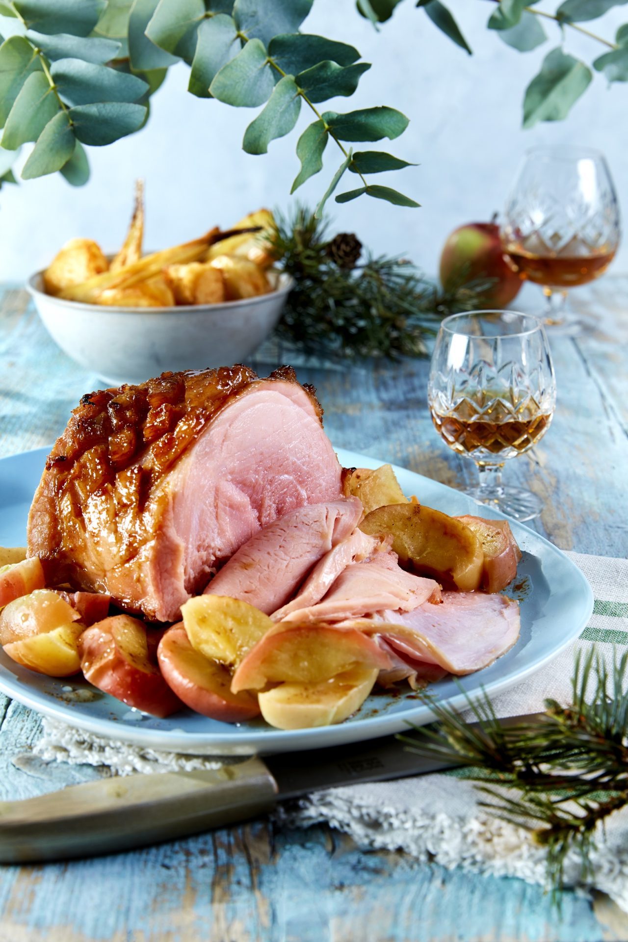 Roast Gammon in cider with calvados and apples with some glasses of whiskey on a blue table