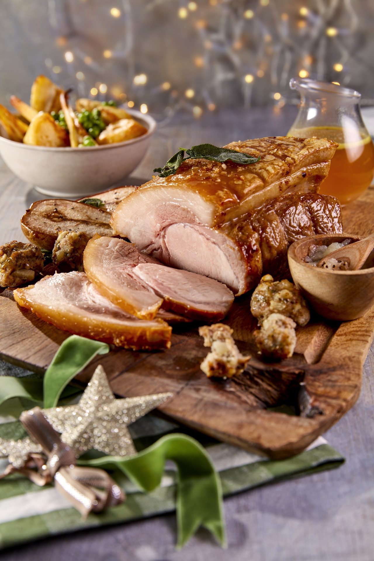 Roast leg of pork served on a wooden chopping board, festive themed décor with side dishes