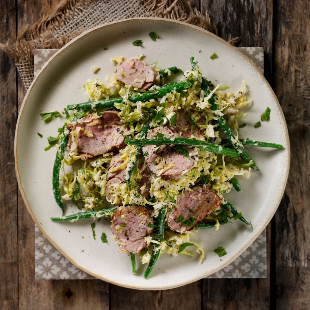 Sliced pork fillet with green vegetable salad on a white dish