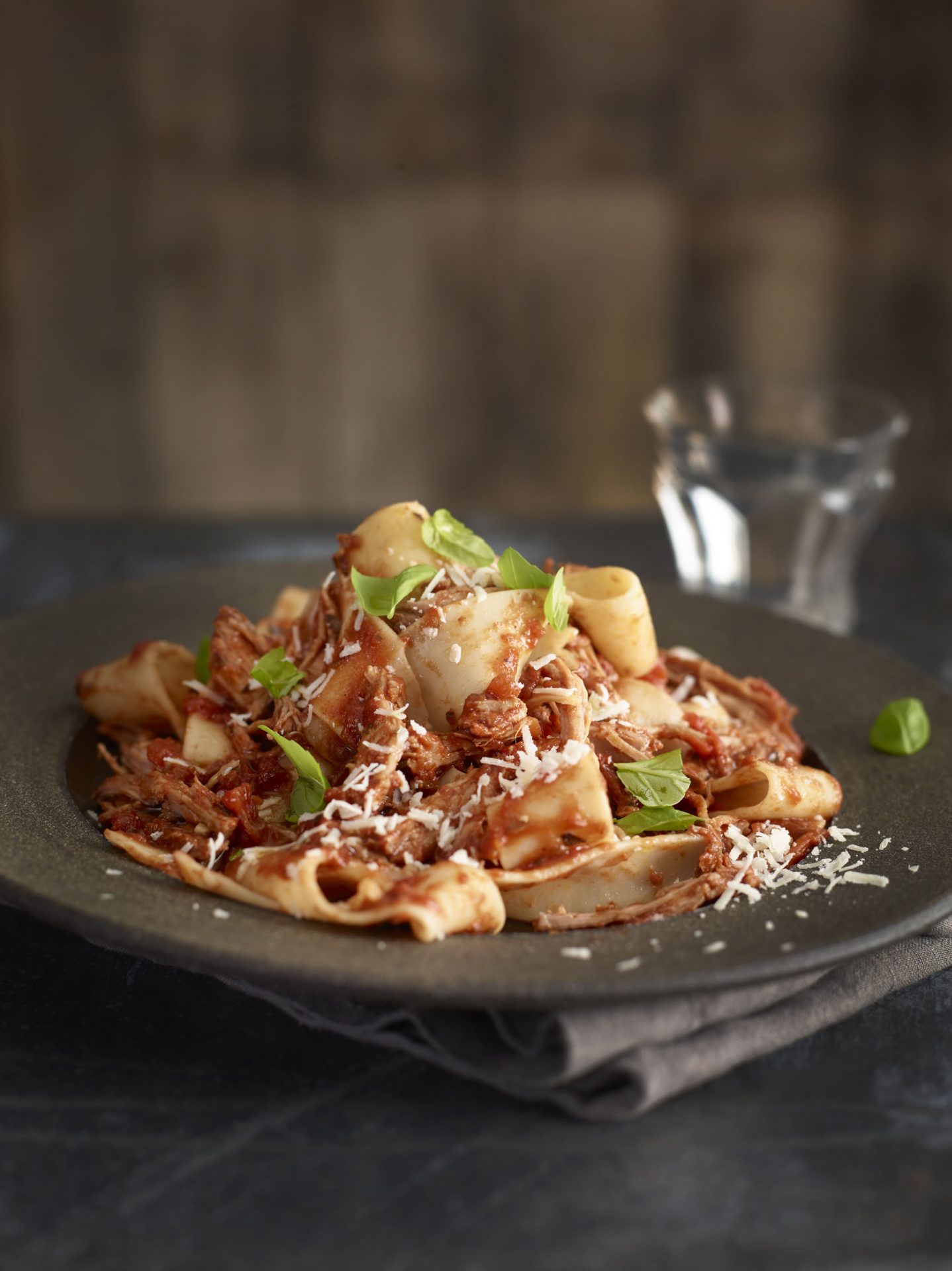 Pulled Pork ragu pasta on a plate with a glass of water in the distance