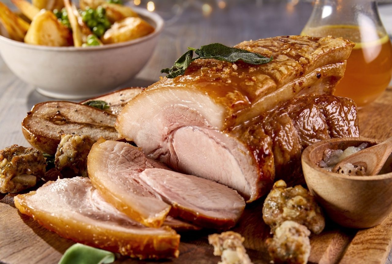 Roast leg of pork served on a wooden chopping board, festive themed décor with side dishes