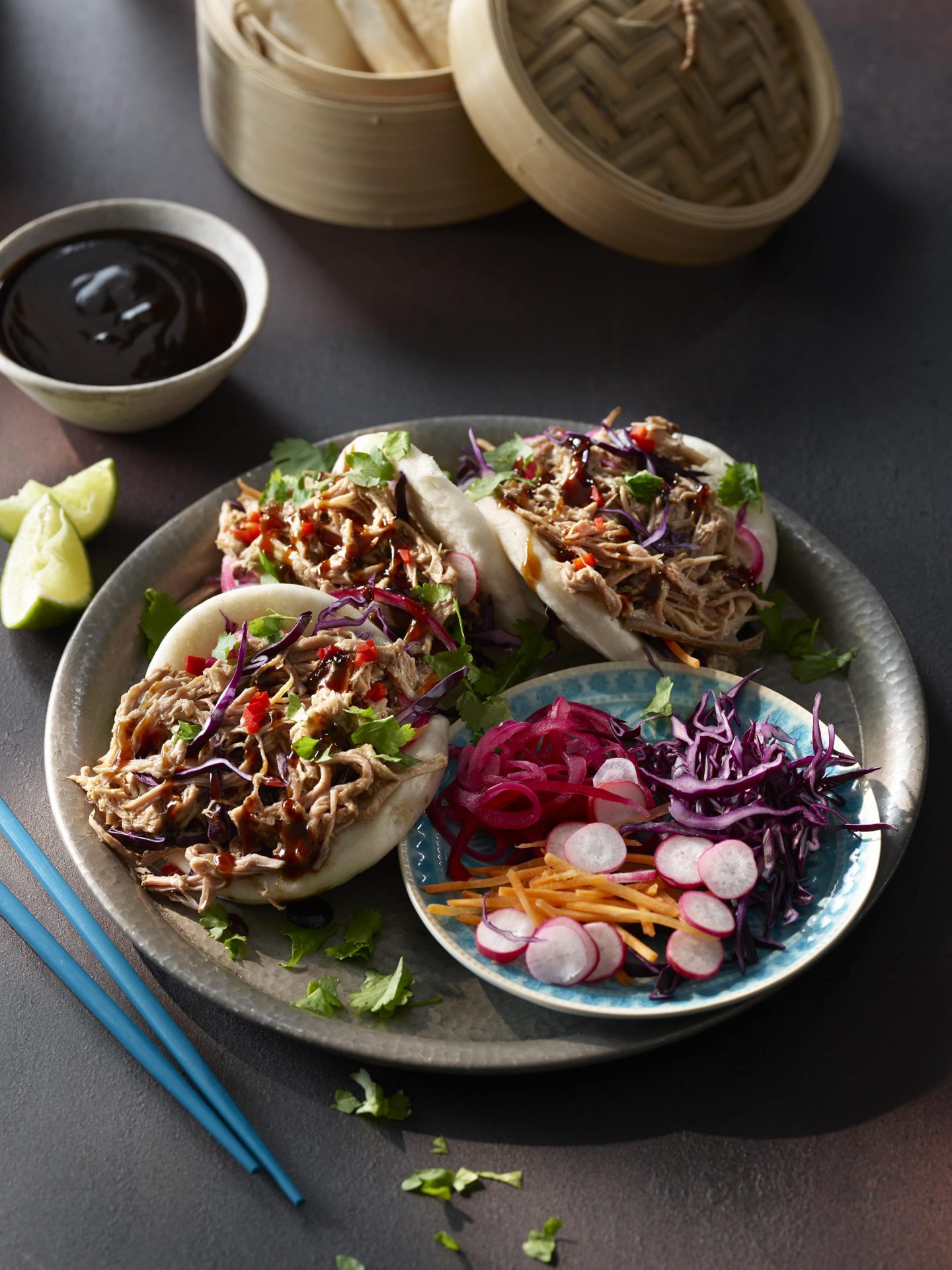 Three bao buns filled with pulled pork and slaw, on a grey dish