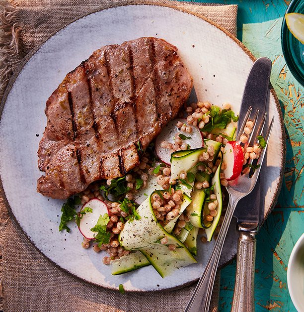 Grilled pork steak with courgette salad on a white plate with cutlery