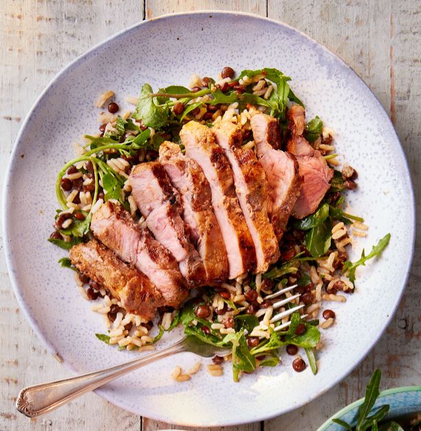 Sliced pork on a bed of salad, on a white plate.