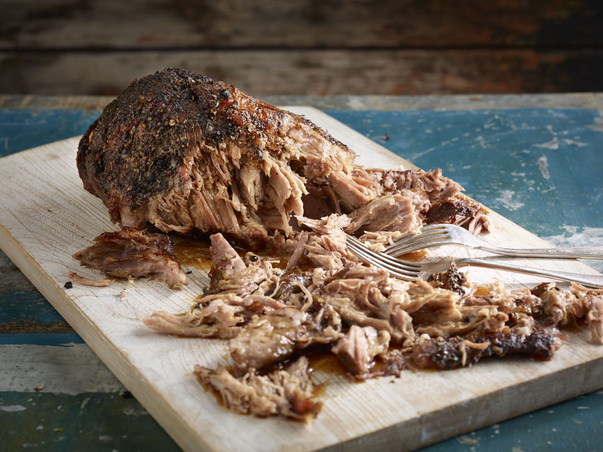 Pulled pork joint, some pulled, on a chopping board with forks