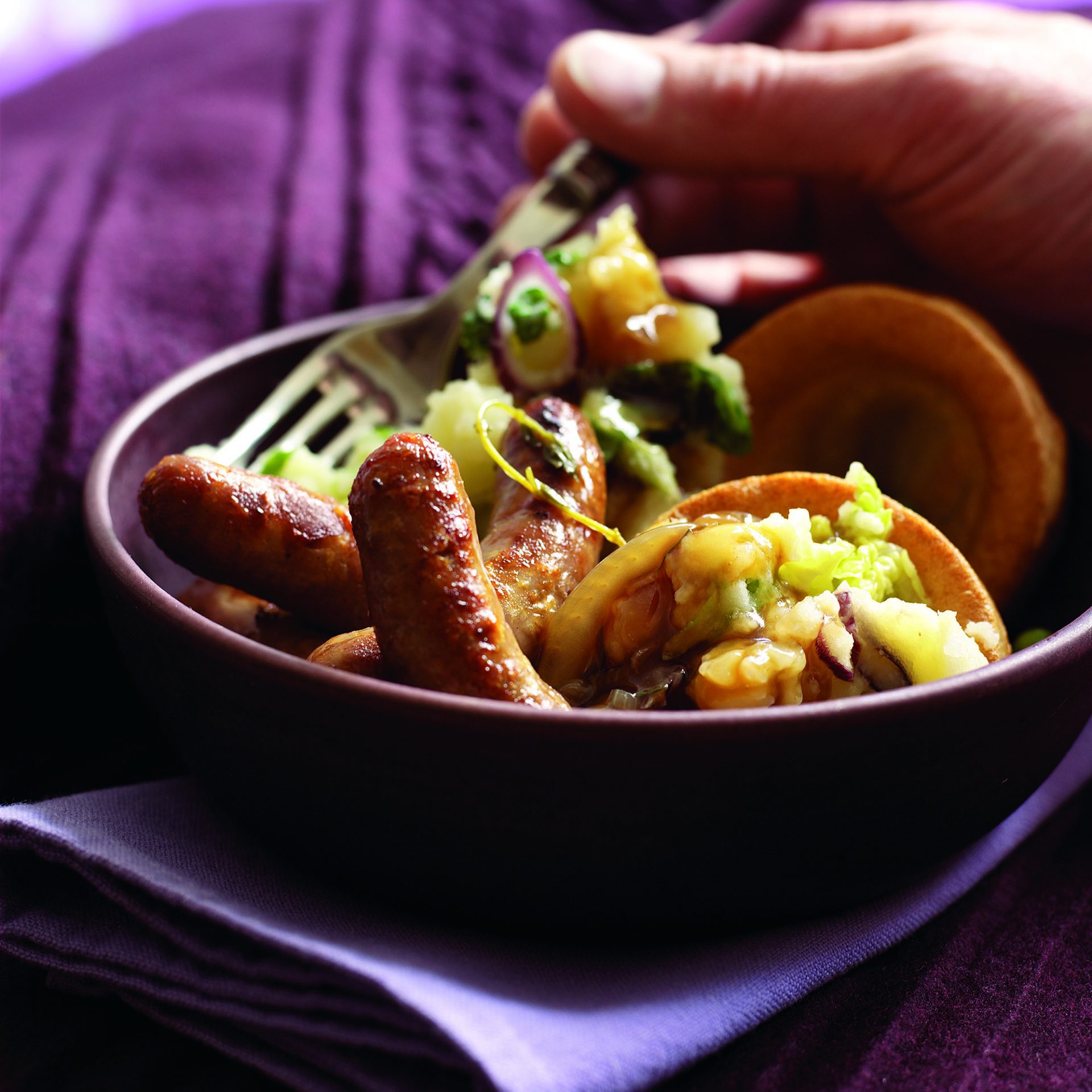 Sausages with colcannon mash in a dark bowl with fork in hand