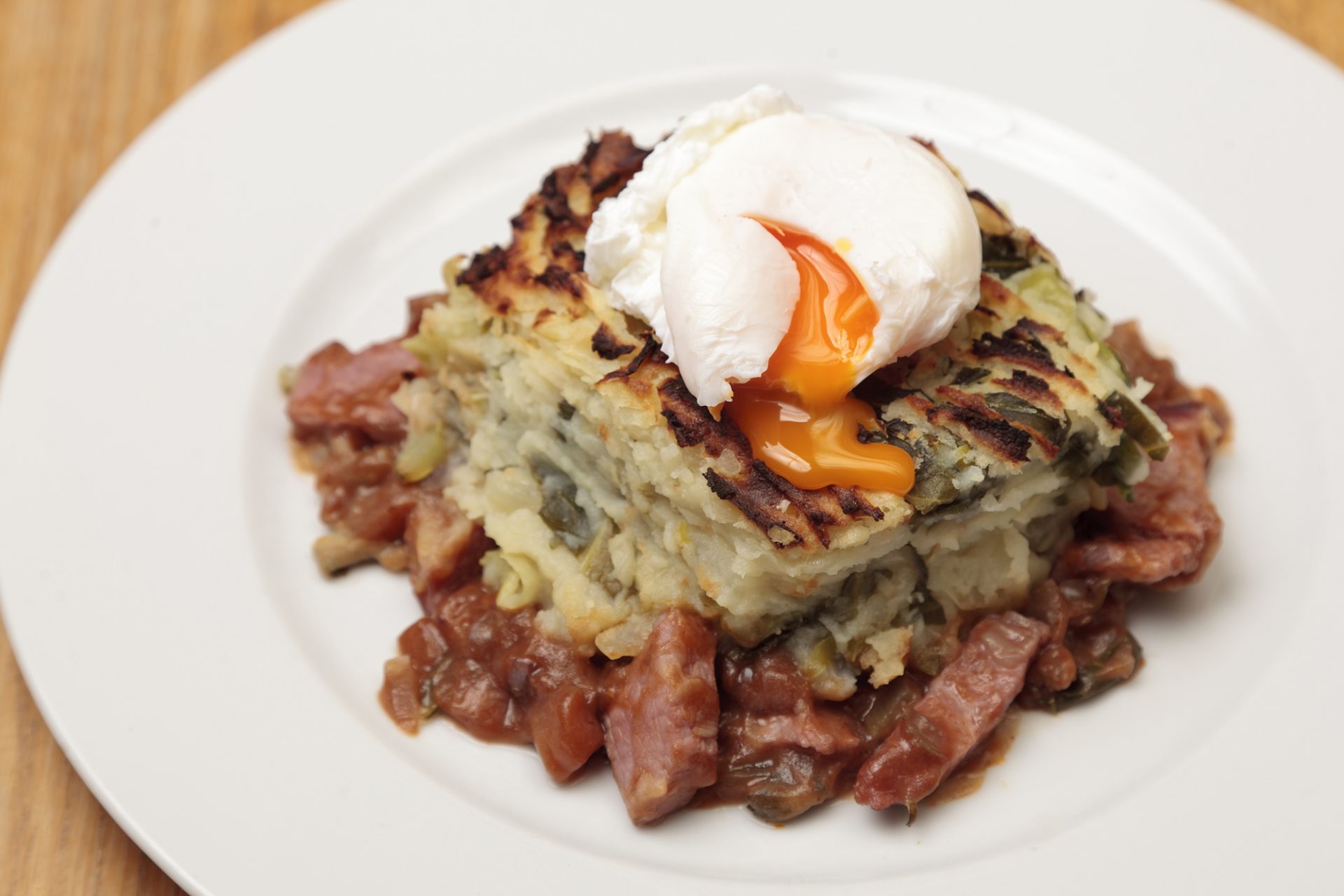 Serving of bubble and squeak on a white plate with an egg on top