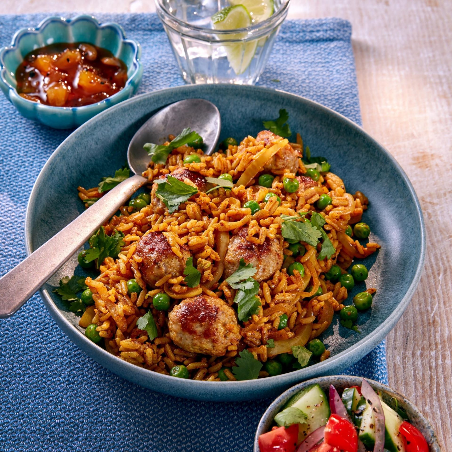 Blue bowl with a spoon, filled with rice and sausage balls and peas