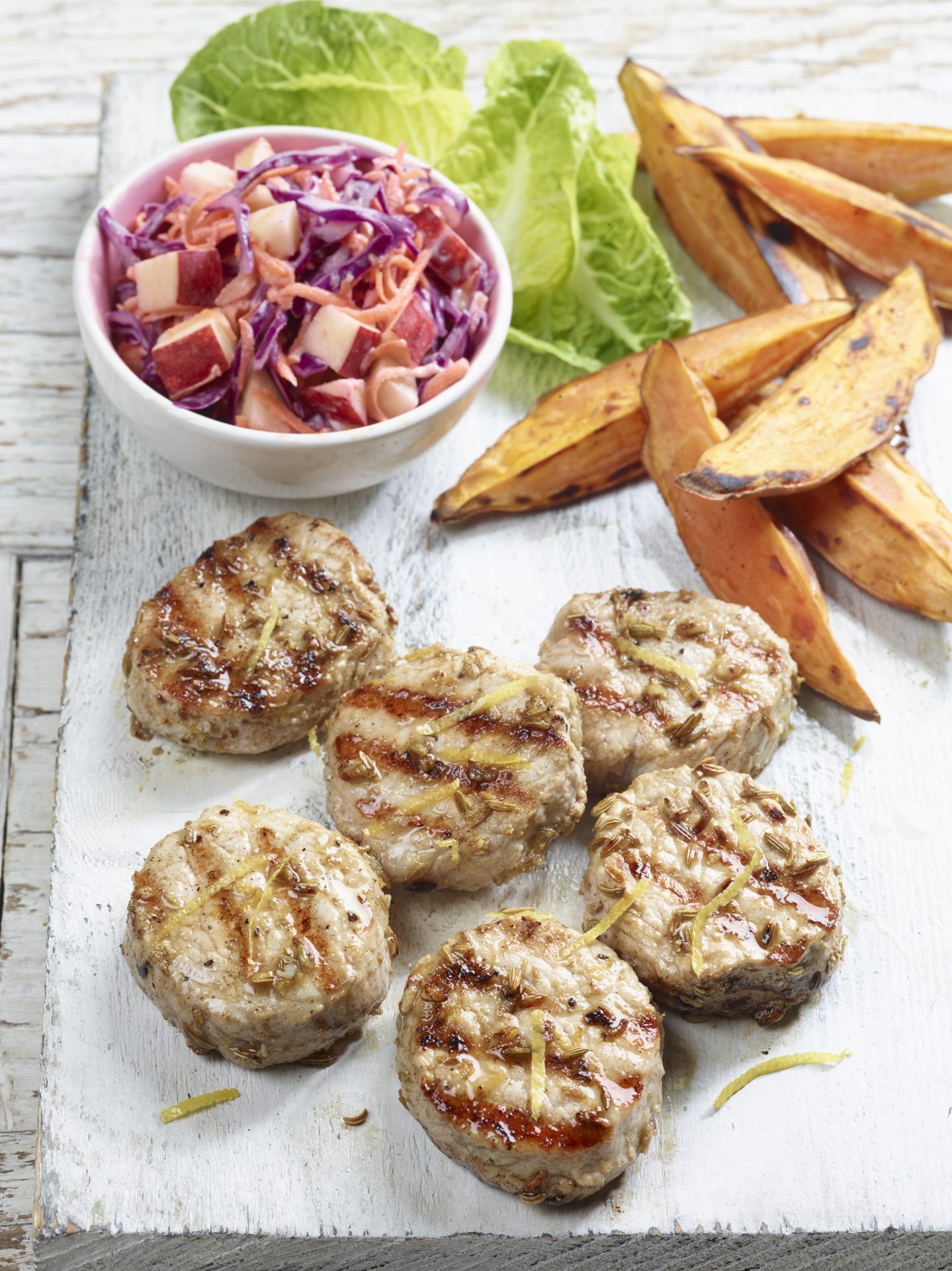 Six pork fillet medallions on a white board with coleslaw and wedges