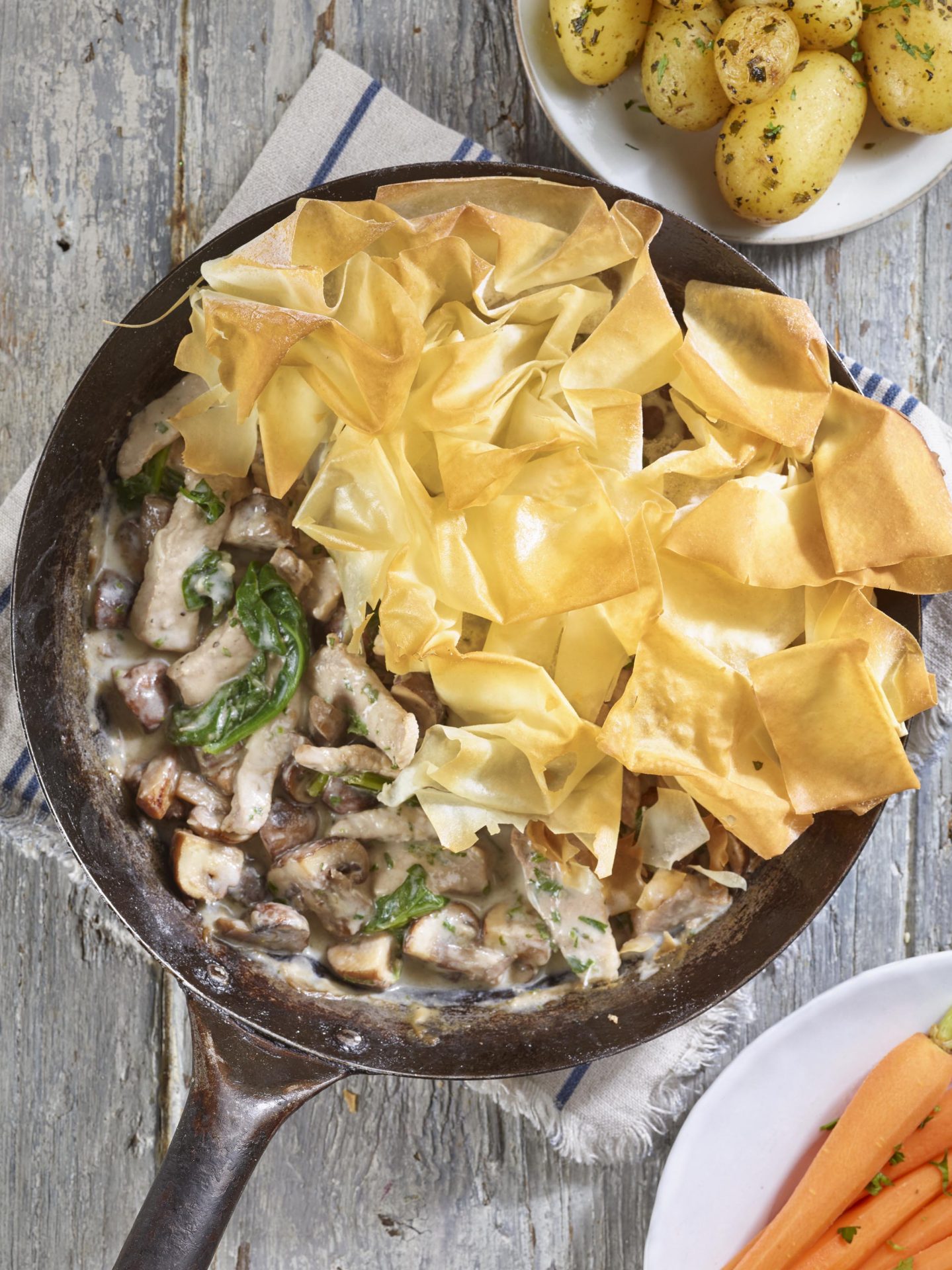 Large black pan filled with mushroom filling and topped with filo pastry