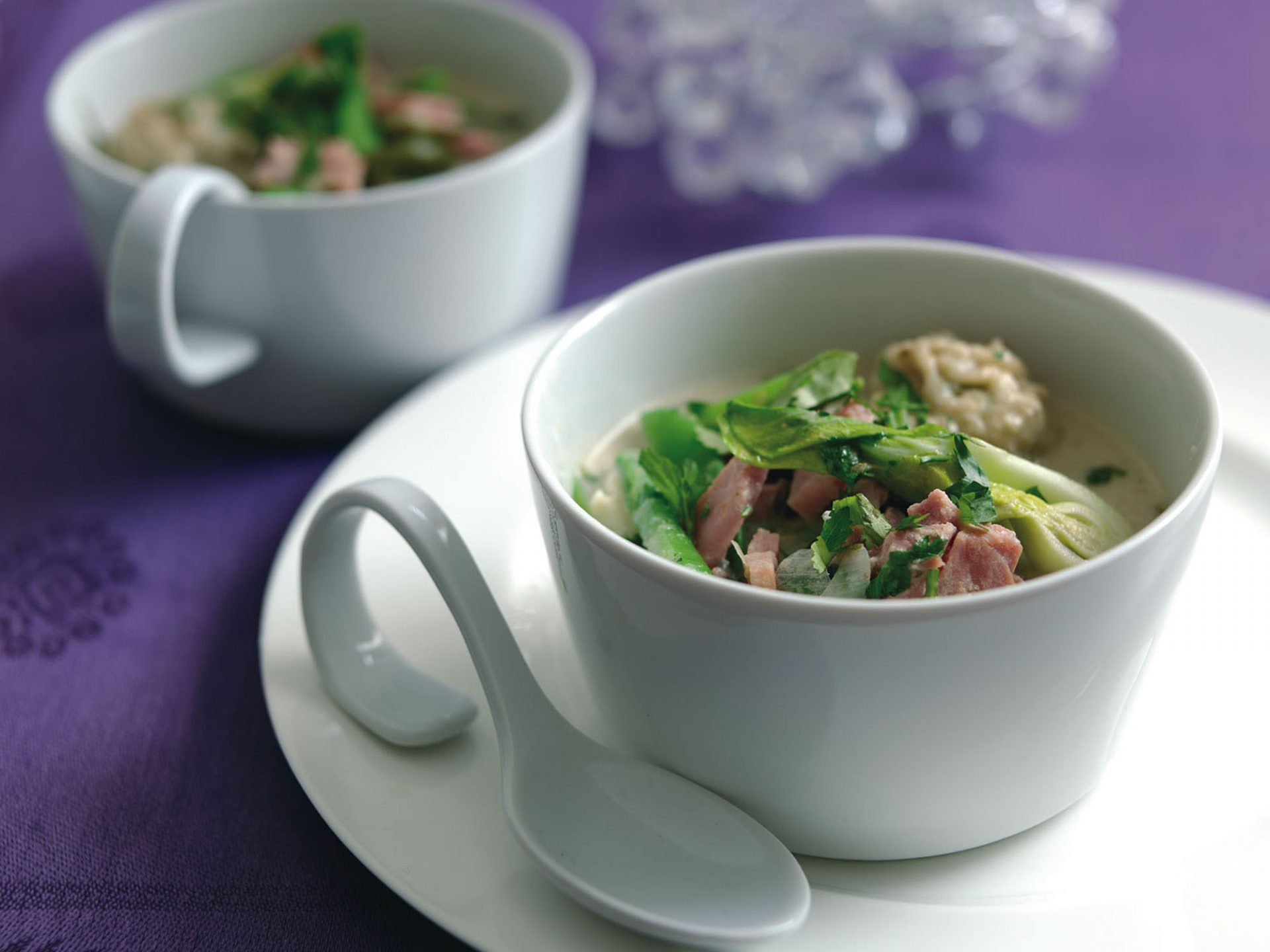 Small white bowl filled with gammon thai green broth with coriander dumplings, with spoon