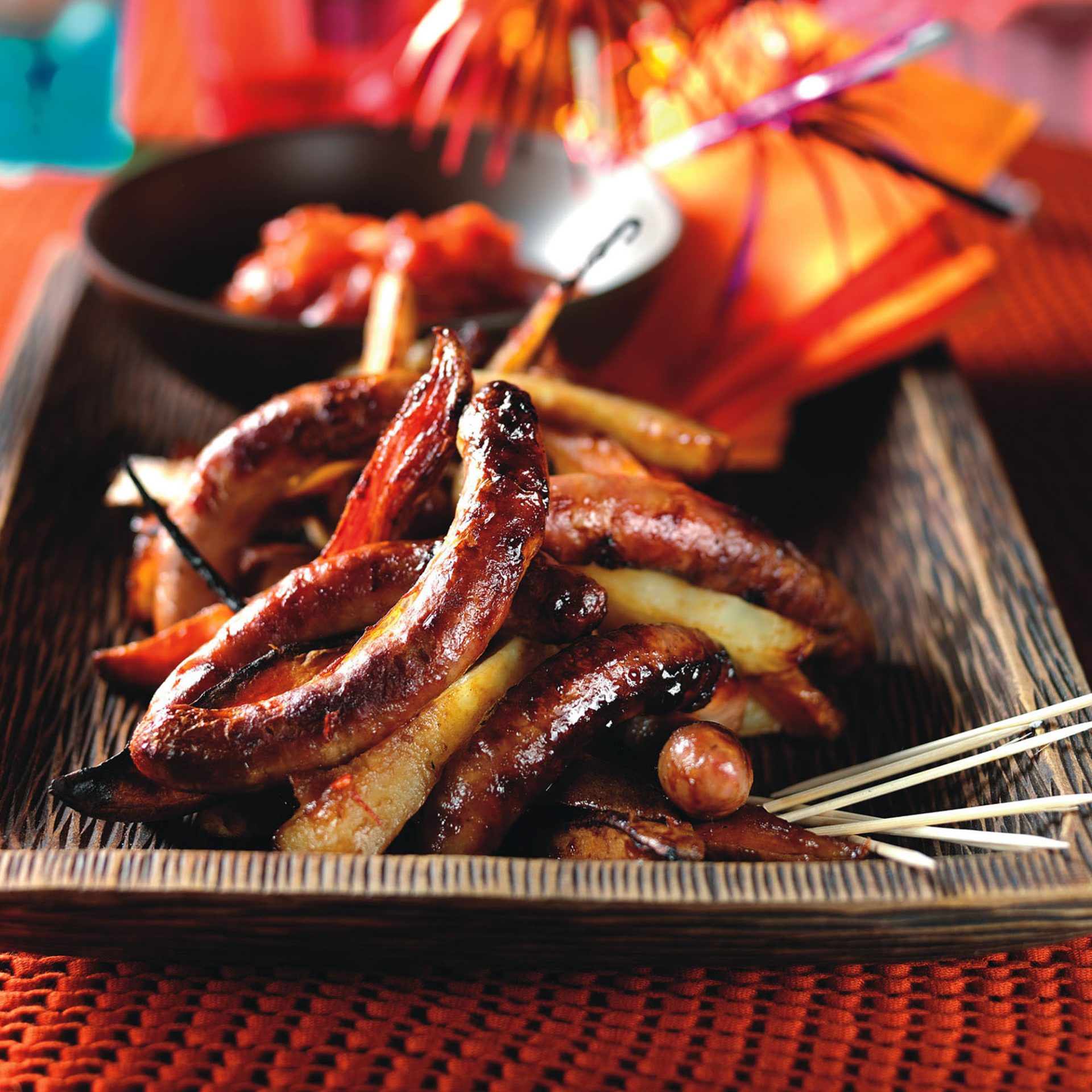 Roasted chipolata sausages with vegetables served on a dark wooden tray