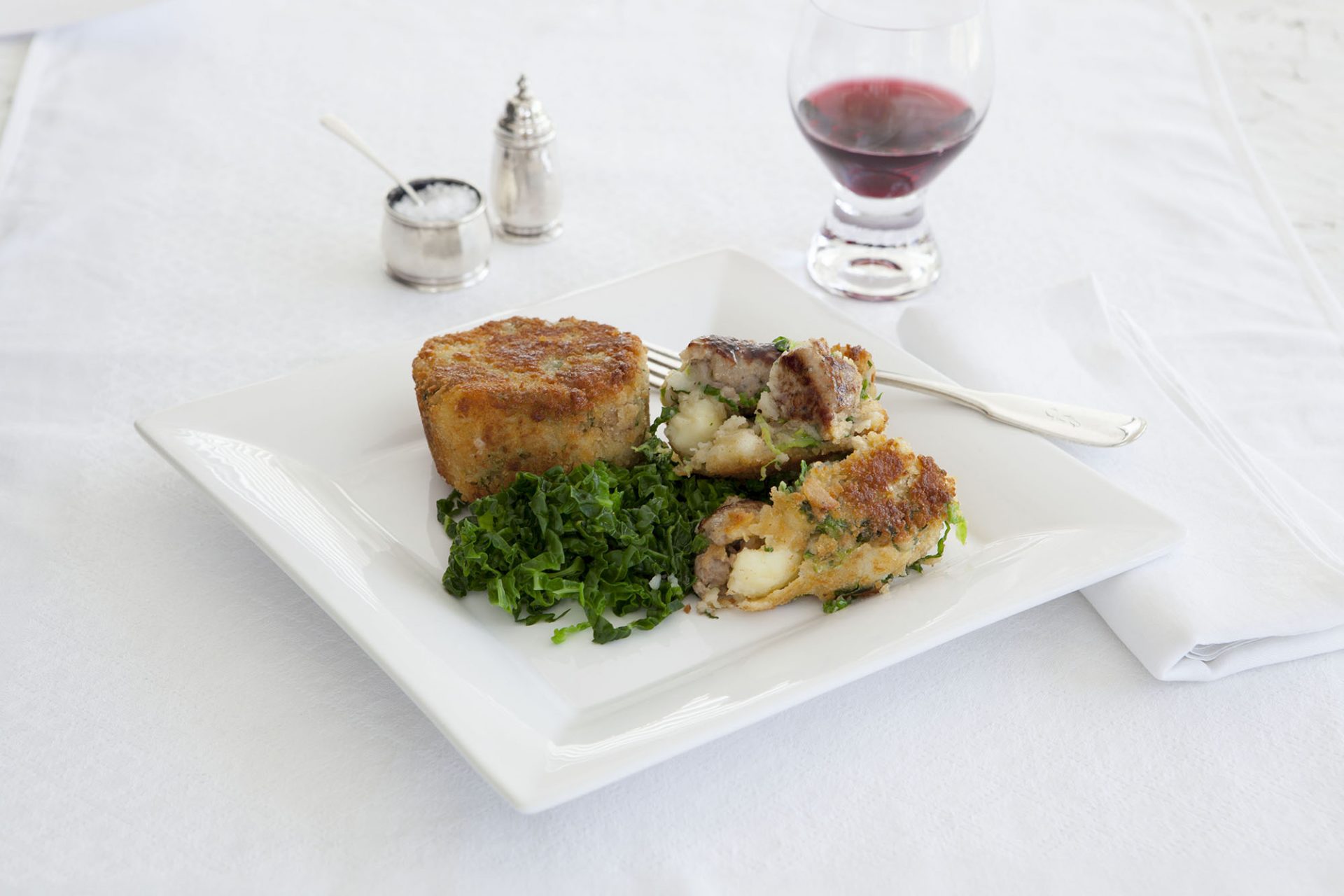 Herby sausage cakes served on a square white plate, wine glass in background.