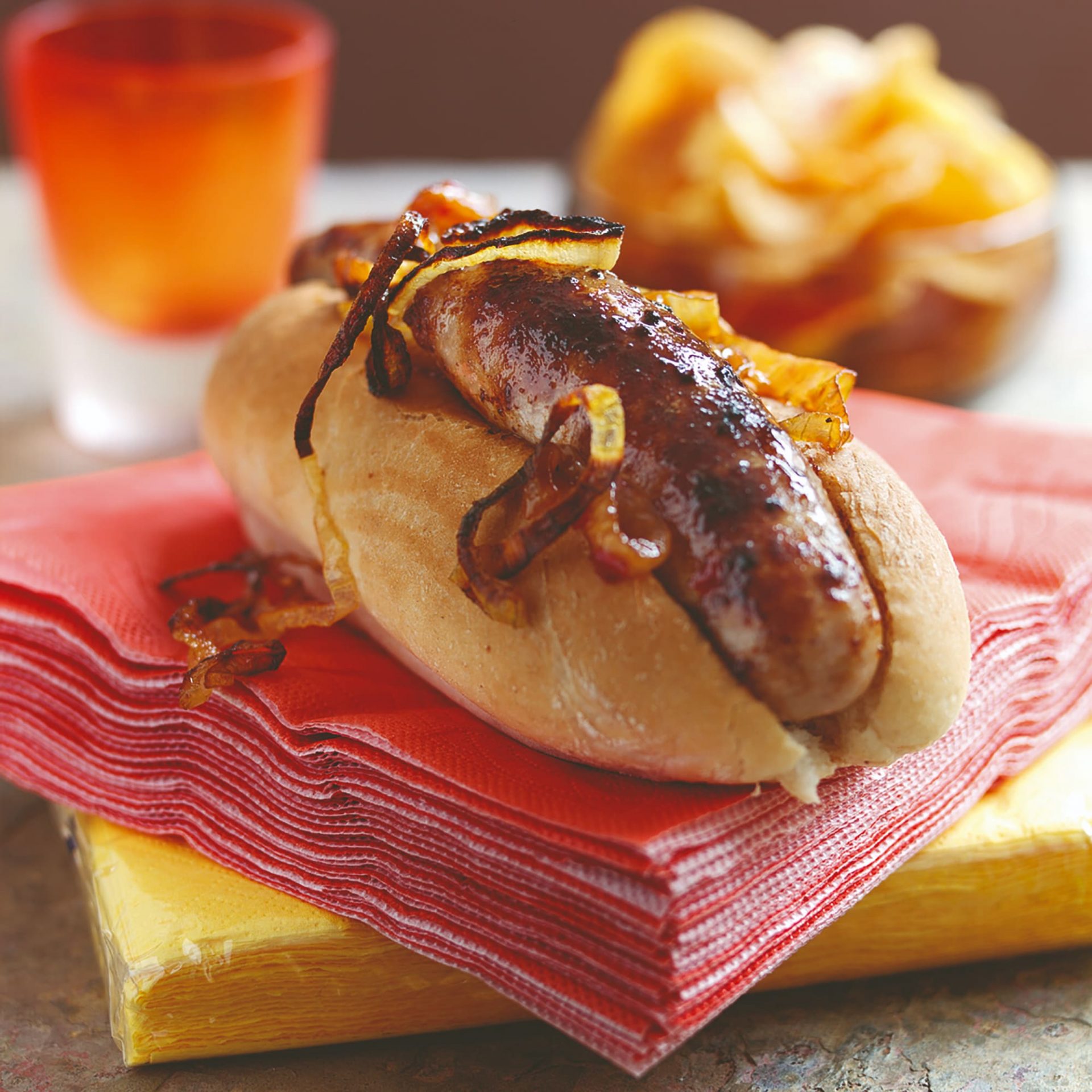 Single hot dog with chilli jam on top of a set of red napkins.