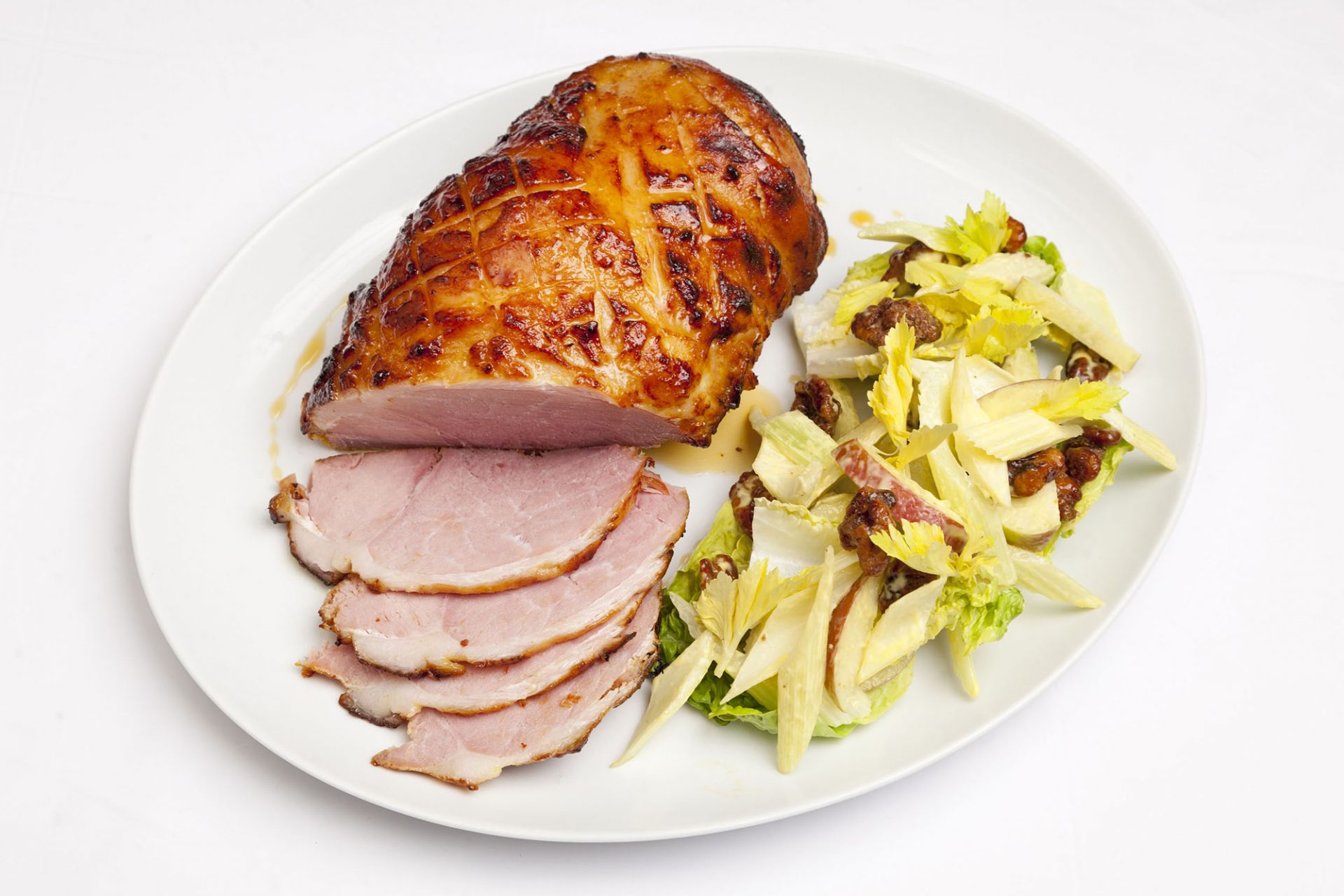 Gammon joint, some sliced, with a waldorf salad, on a white plate