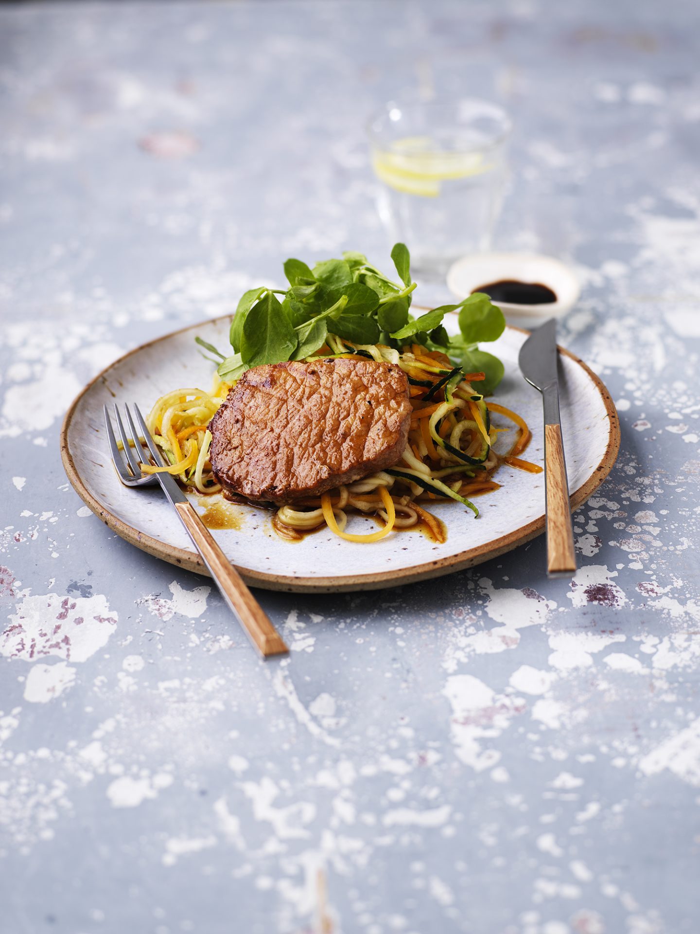 Pork medallion on a bed of vegetable spaghetti, with cutlery.