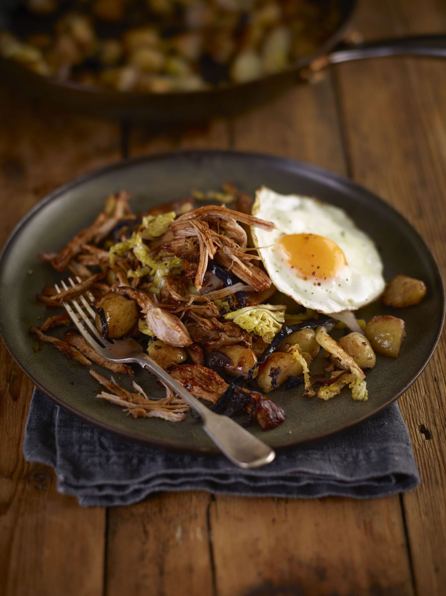 Pulled pork hash with cabbage and fried egg served on a black plate, with fork