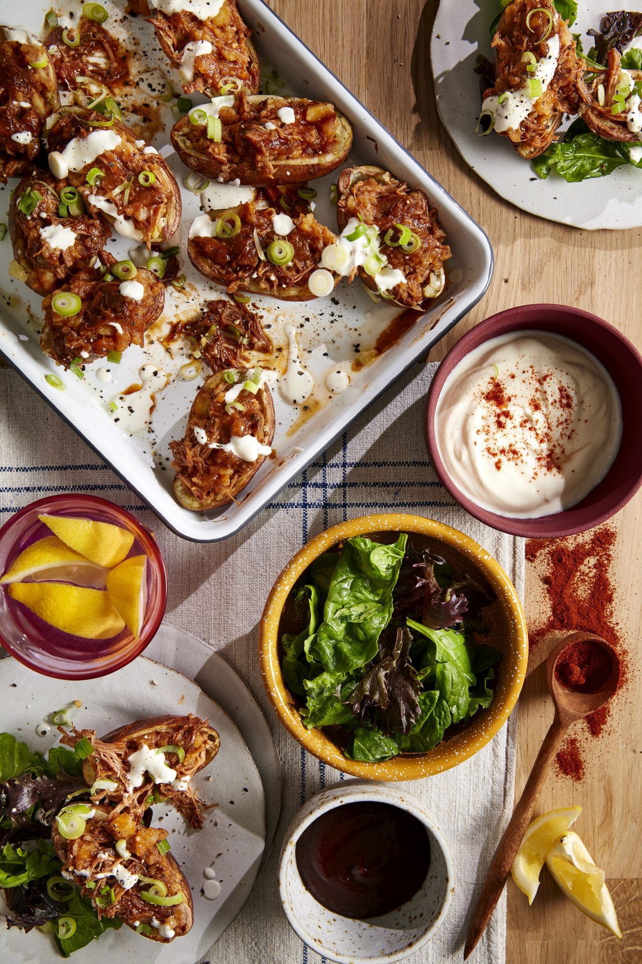 Pulled pork topped potato skins served in a baking tray, with dips and lemon wedges in bowls on side.