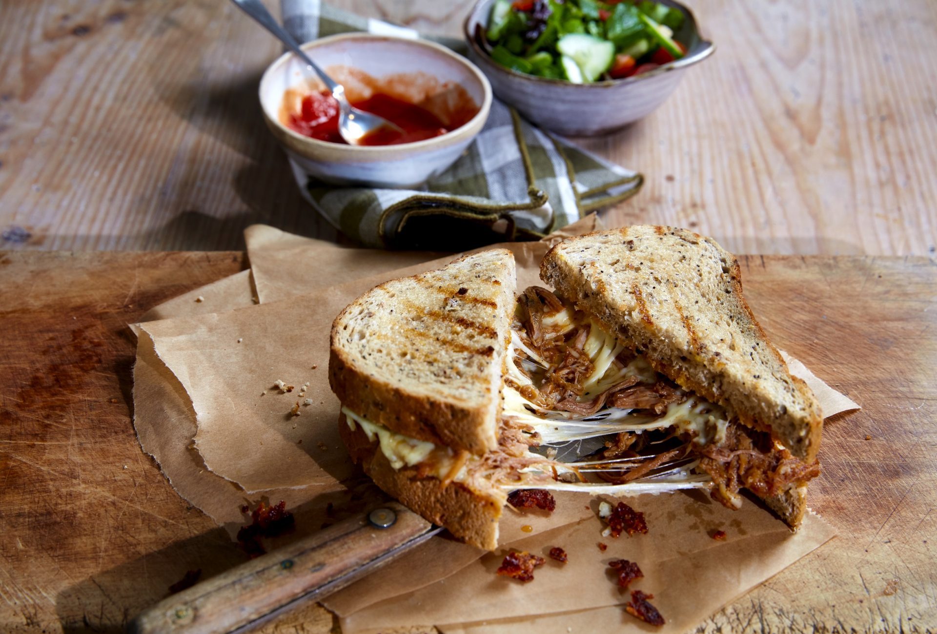 Sliced pulled pork filled toastie on a wooden board, with cheese pull