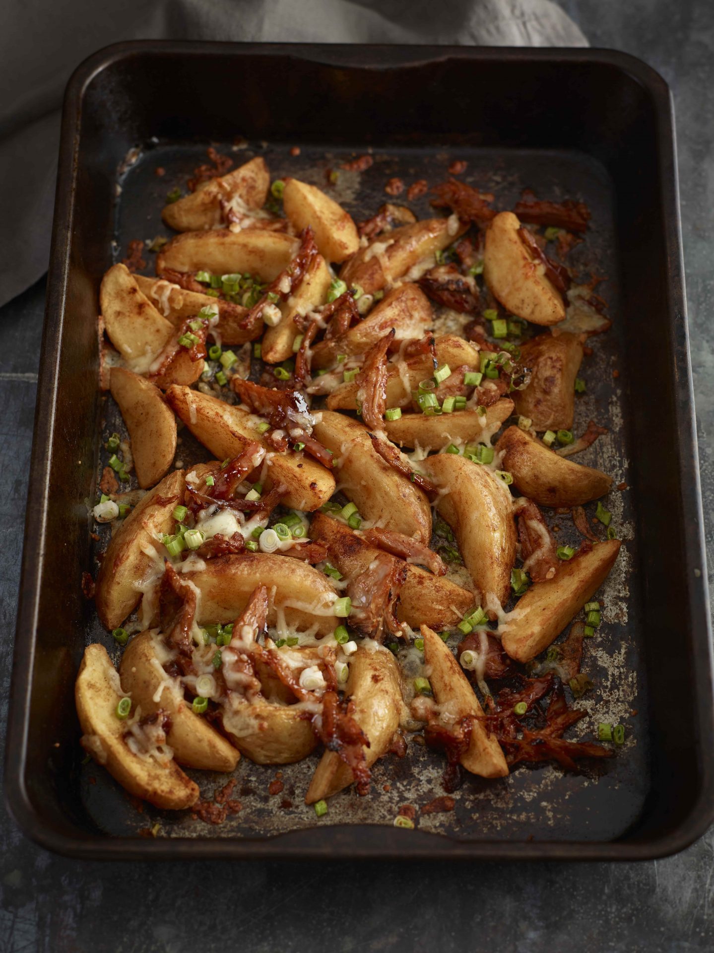 Large black baking tray filled with wedges beans and pulled pork