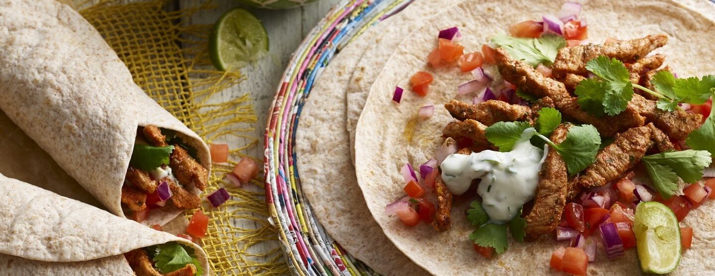 Flat tortilla with pork fajita fillings, plus three ready-made fajitas. Side dip in a bowl on side.