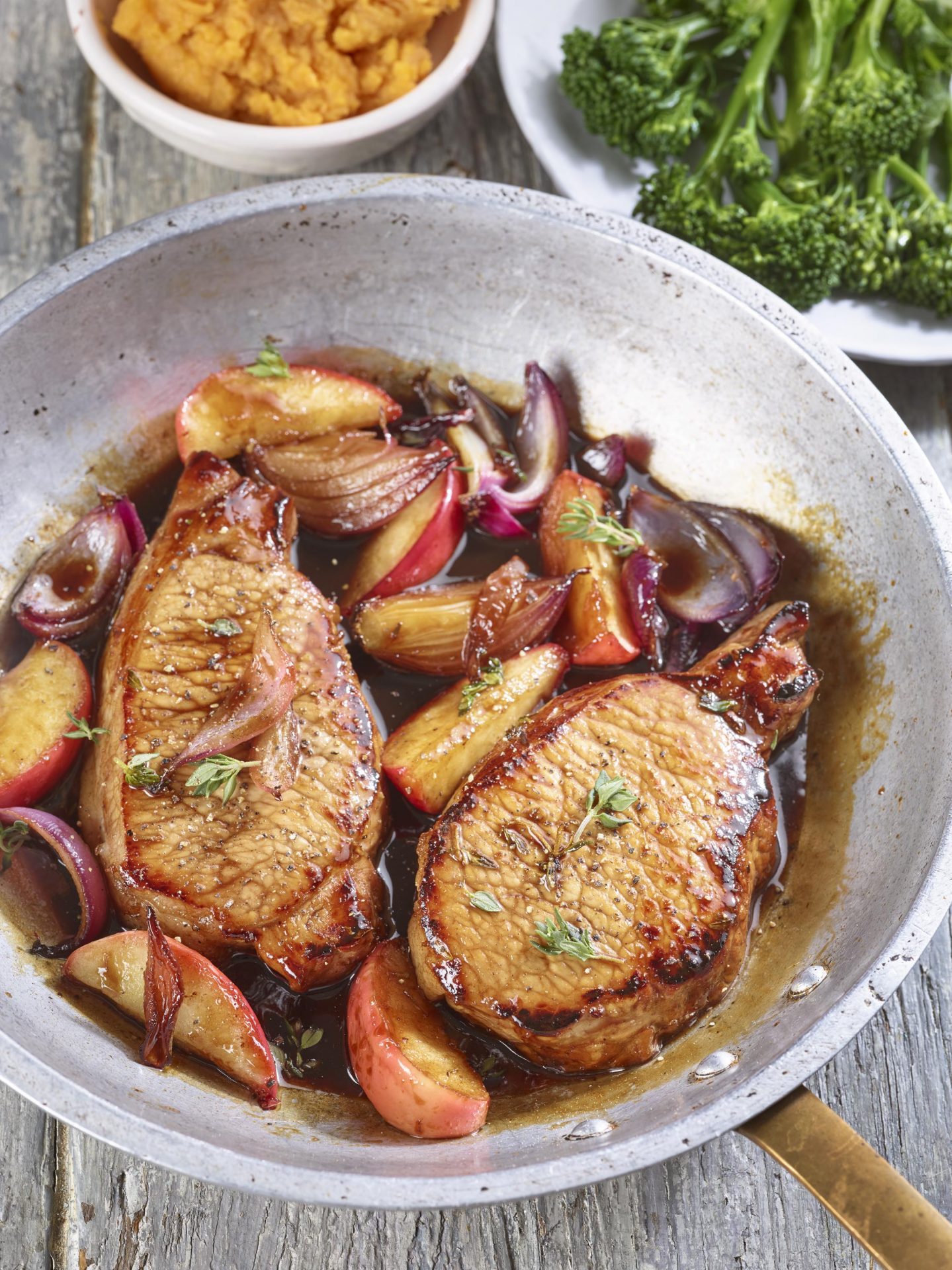 Two pork chops with apples in a balsamic sauce, in a metal frying pan