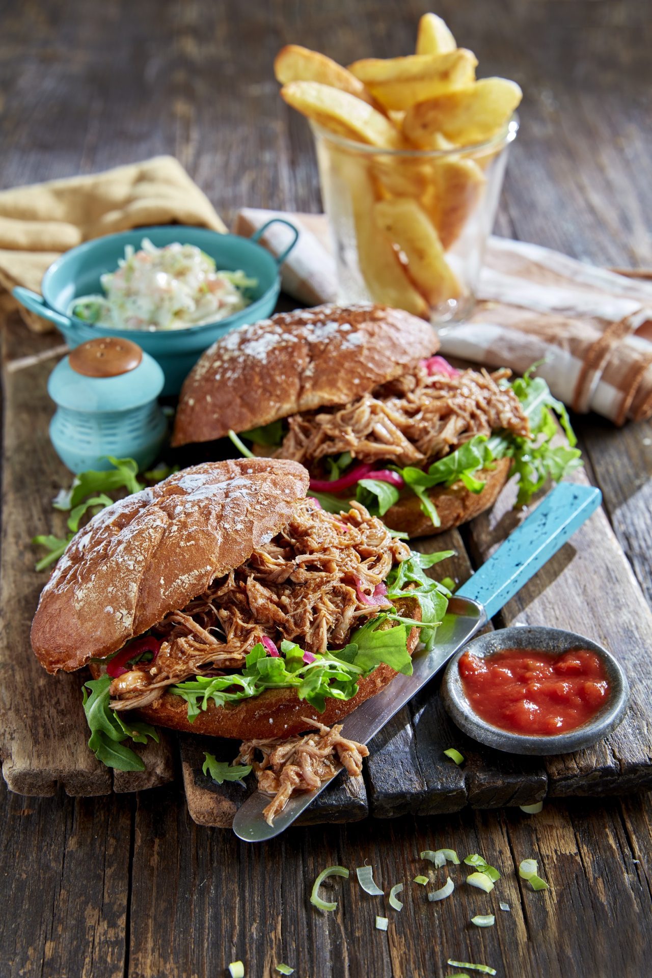 Two burger buns filled with pulled pork and lettuce, on a chopping board.