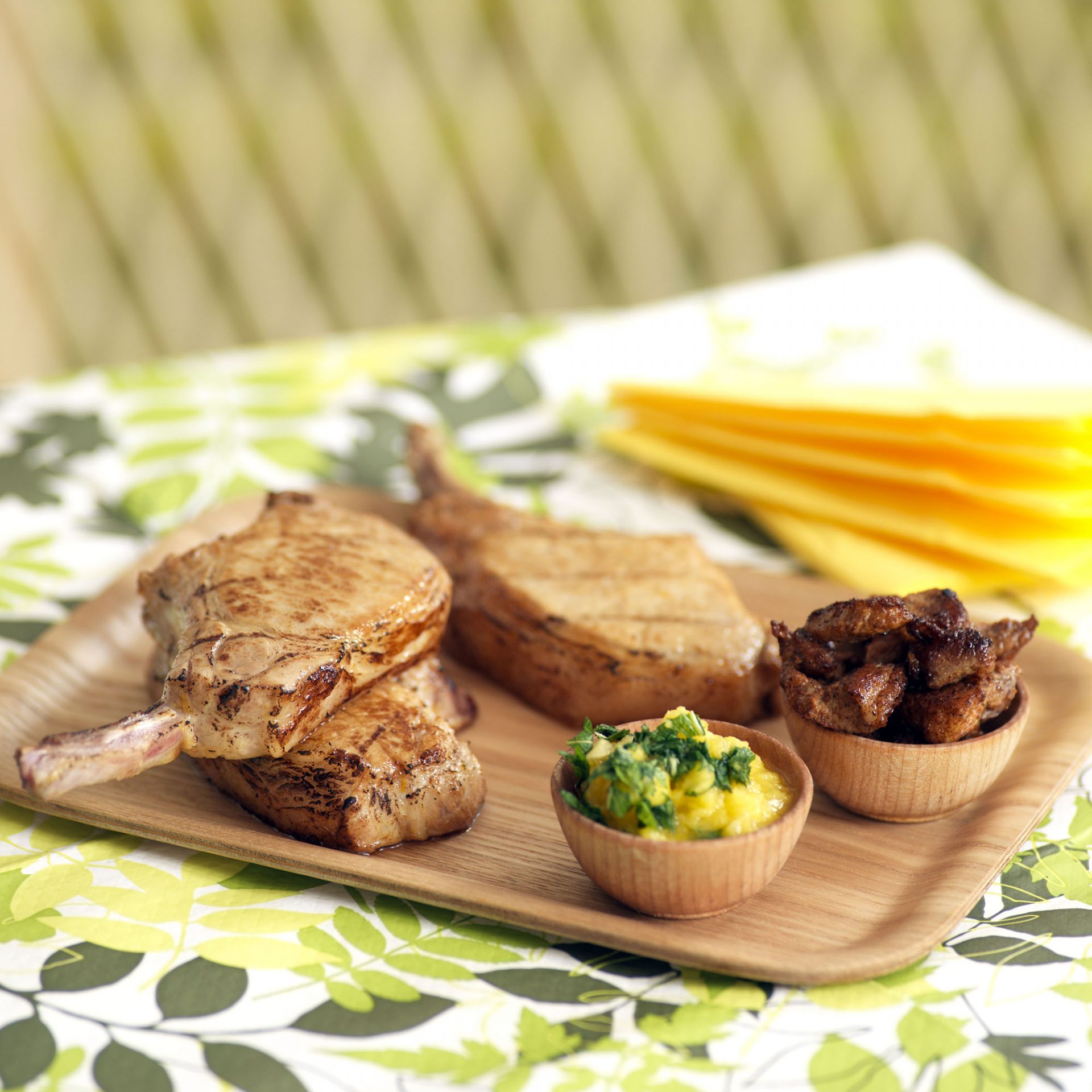 Three pork chops served on a wooden tray, with sides.