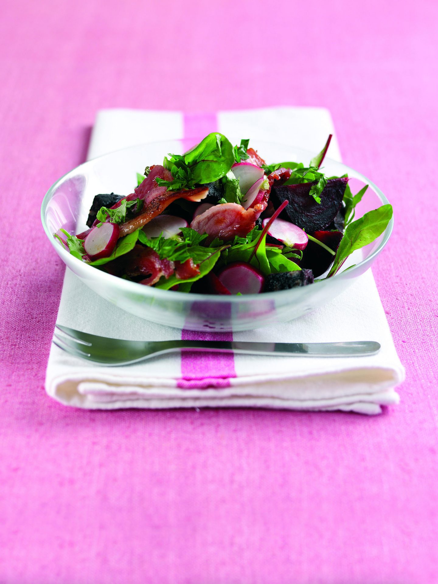 Maple cured bacon spring salad served in a clear bowl, on a table cloth.