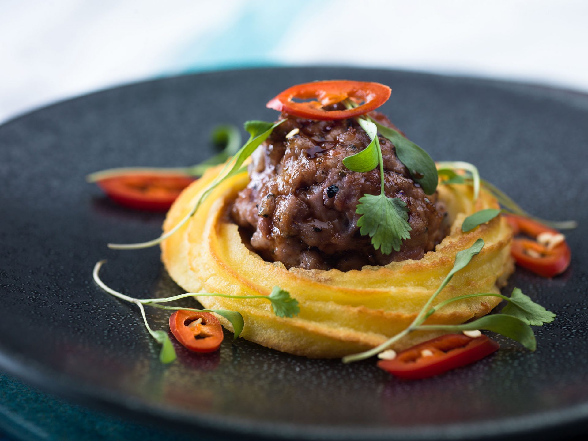 Wasabi duchess potato with honey and soy glazed sausage served on a black plate