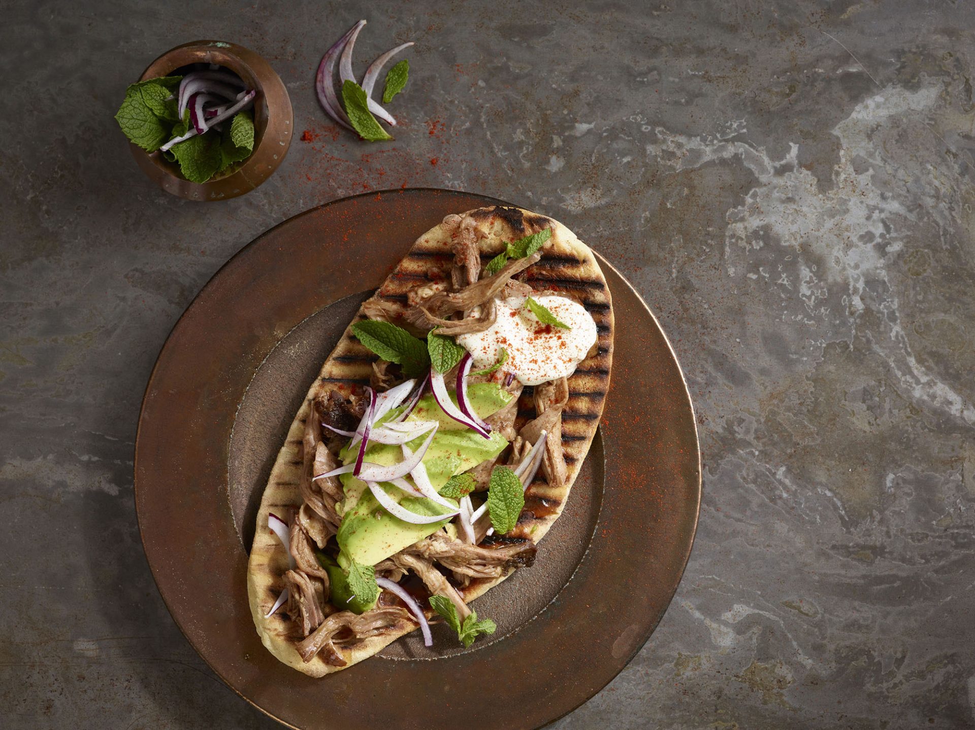 Pulled pork on top of a flatbread, served on a brown plate