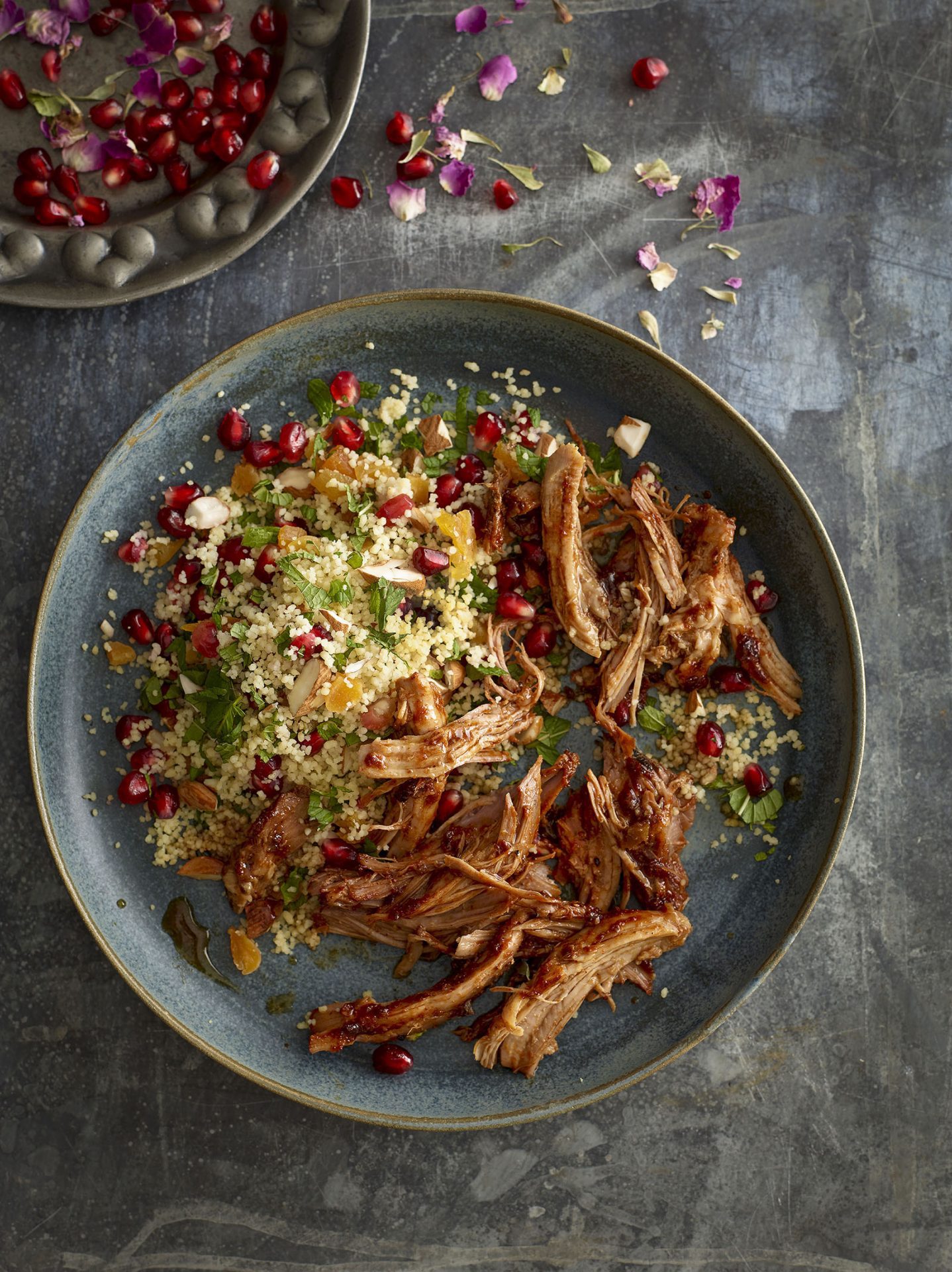 Grey plate with pulled pork and fruity couscous dish, on a slate backdrop