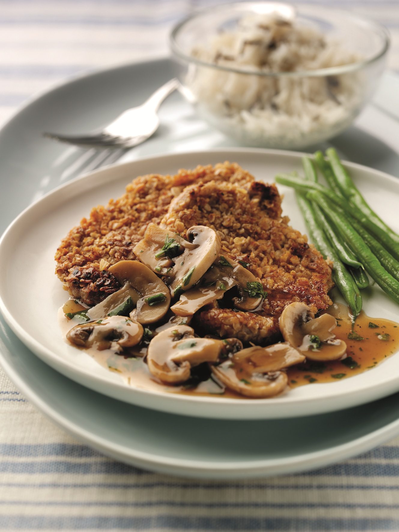 Two oat coated pork with spicy mushroom sauce served on a white plate with green beans