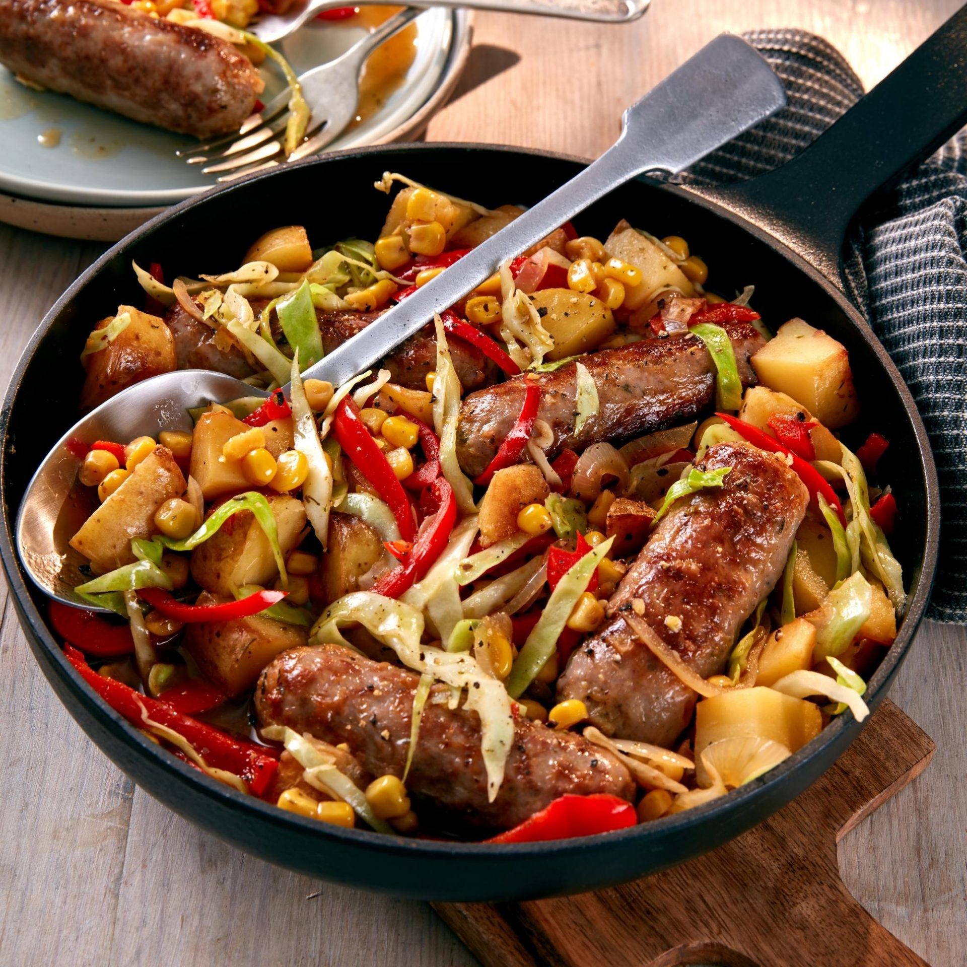 Large black pan with spoon, containing sausage braise dish