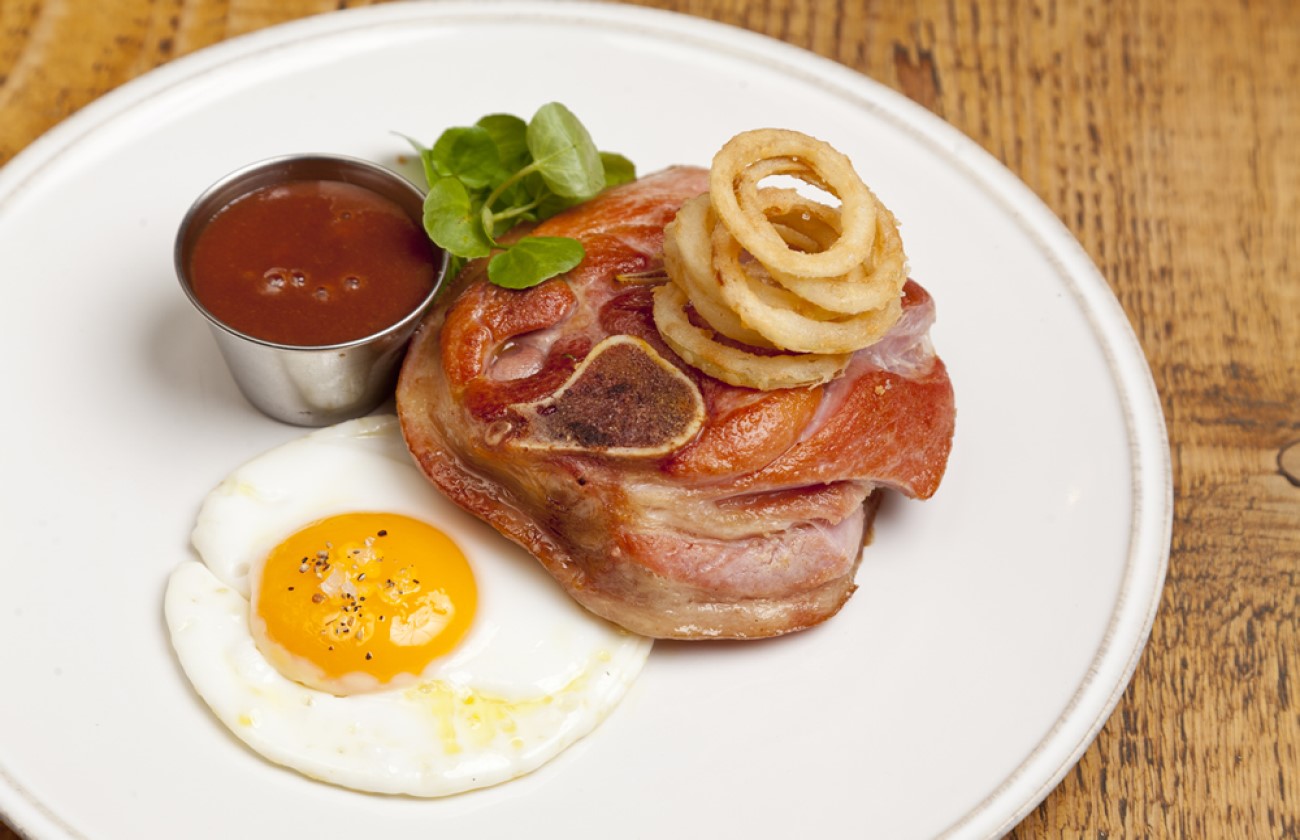 Gammon Osso Bucco served with a fried egg and onion rings on a white plate.