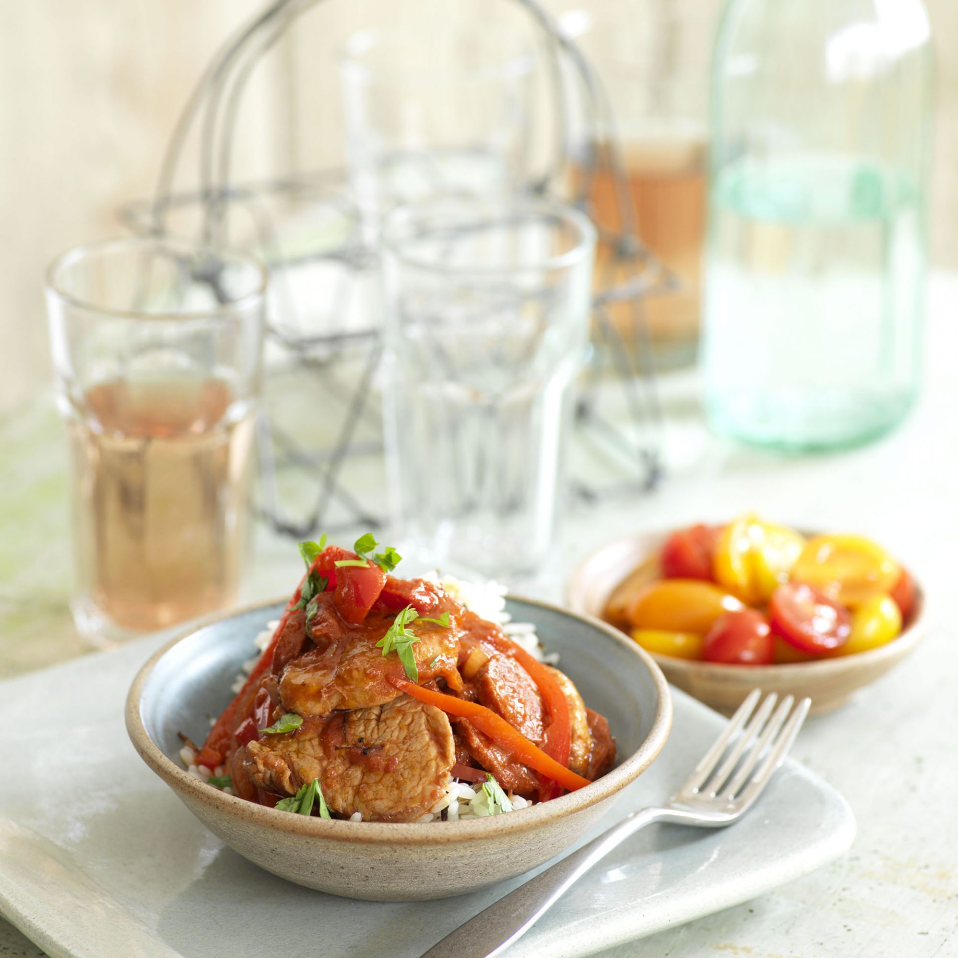 Pan fried pork fillets with chorizo peppers and tomatoes in a bowl on a plate, with a fork on side.