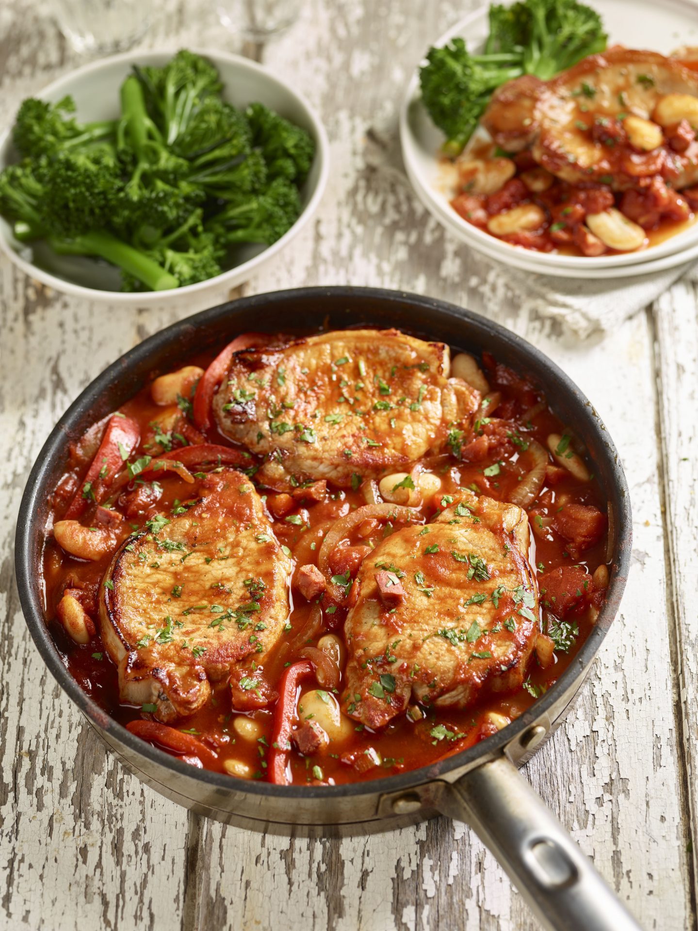 Three pork steaks with butter beans and chorizo in a black frying pan