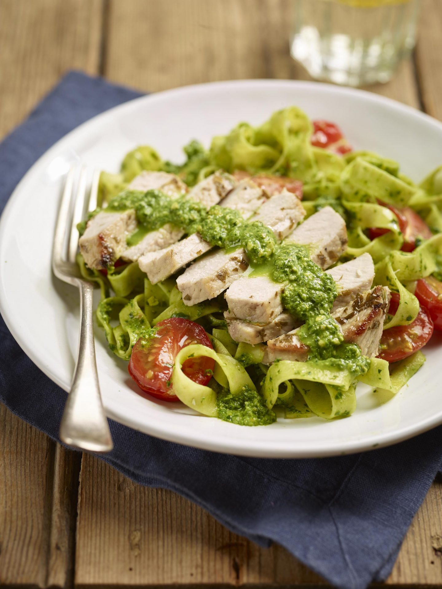 Sliced pork on top of a pesto pasta in a white bowl with fork