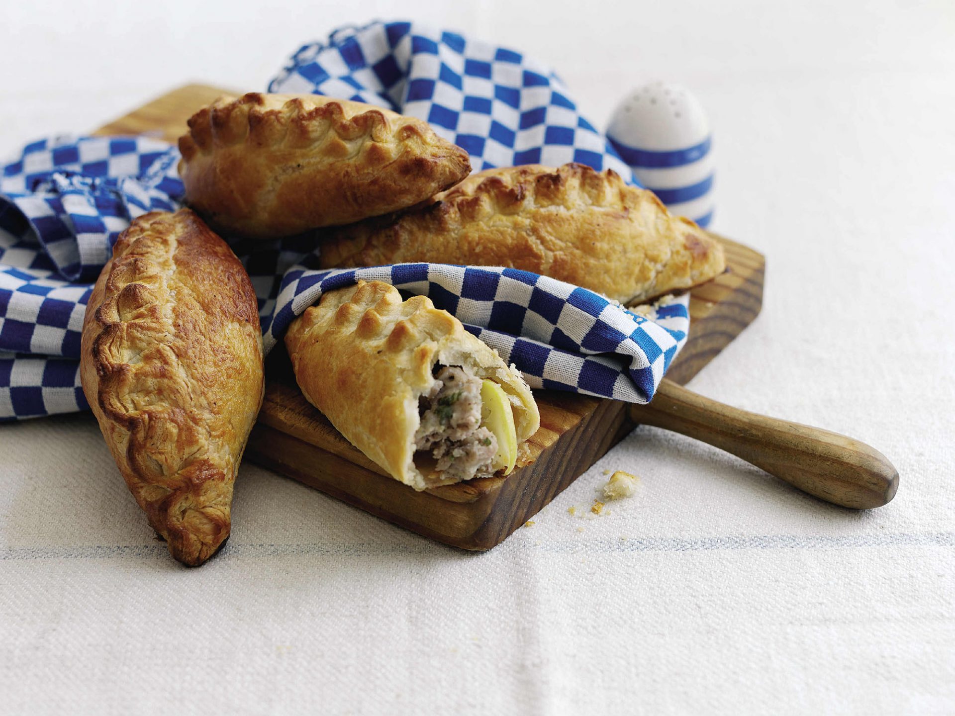 Four mini pasties served on a blue napkin on a wooden board.