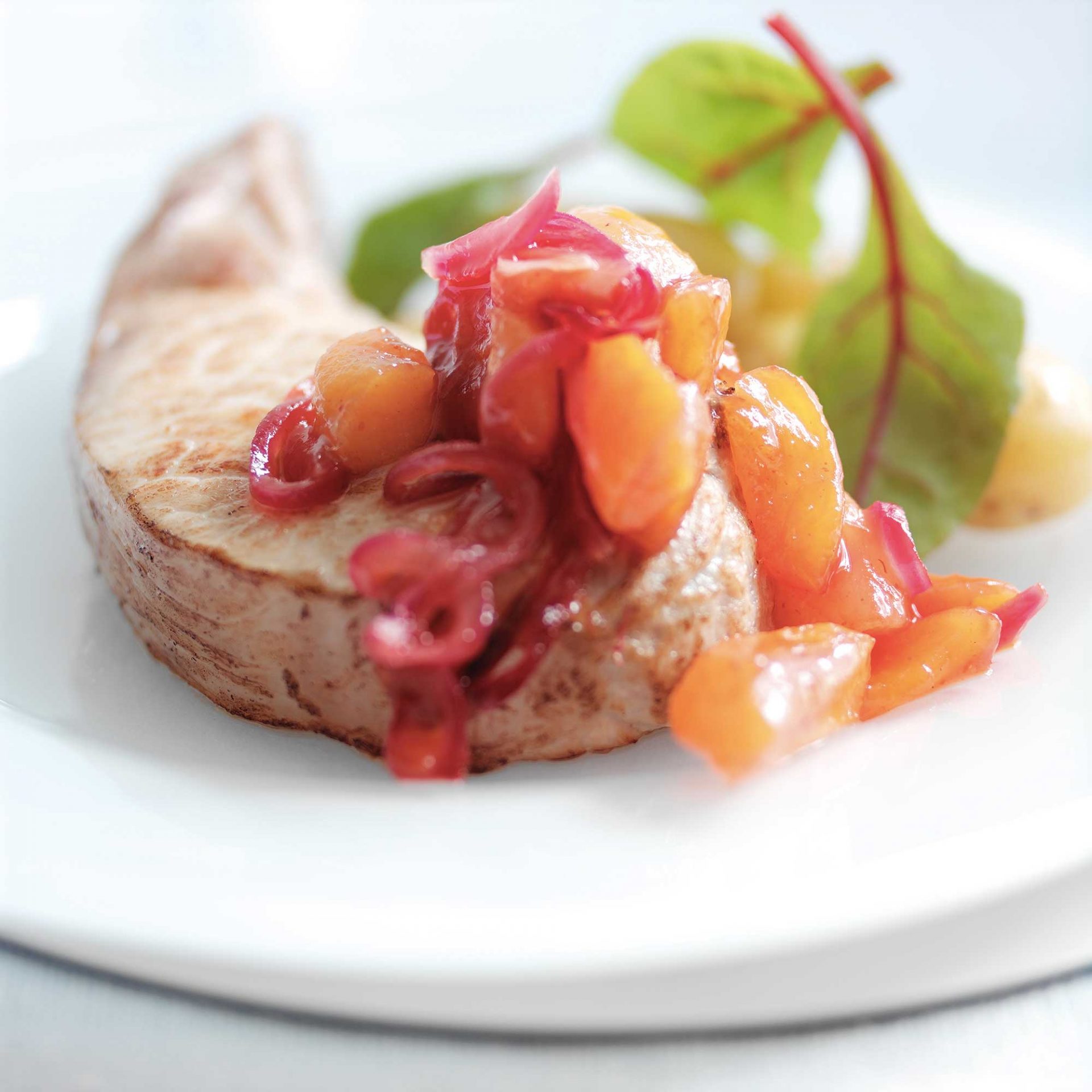 Cooked pork chop with fruity apricot chutney served on a white plate.