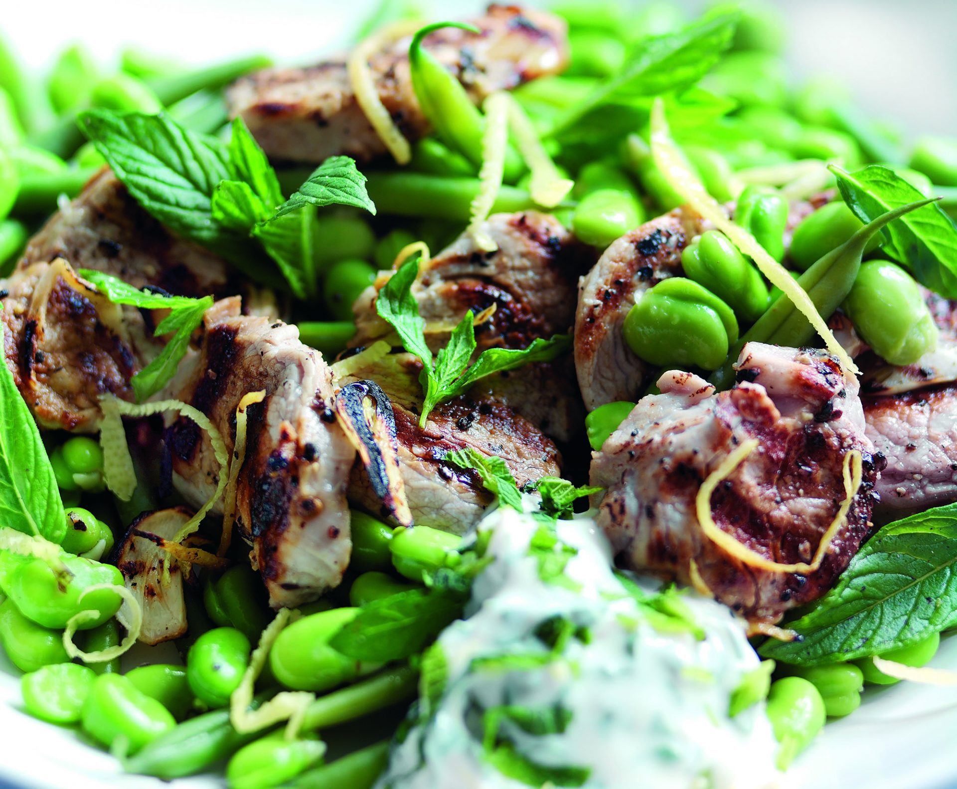 Pork fillet medallions with green bean salad served in a white bowl.