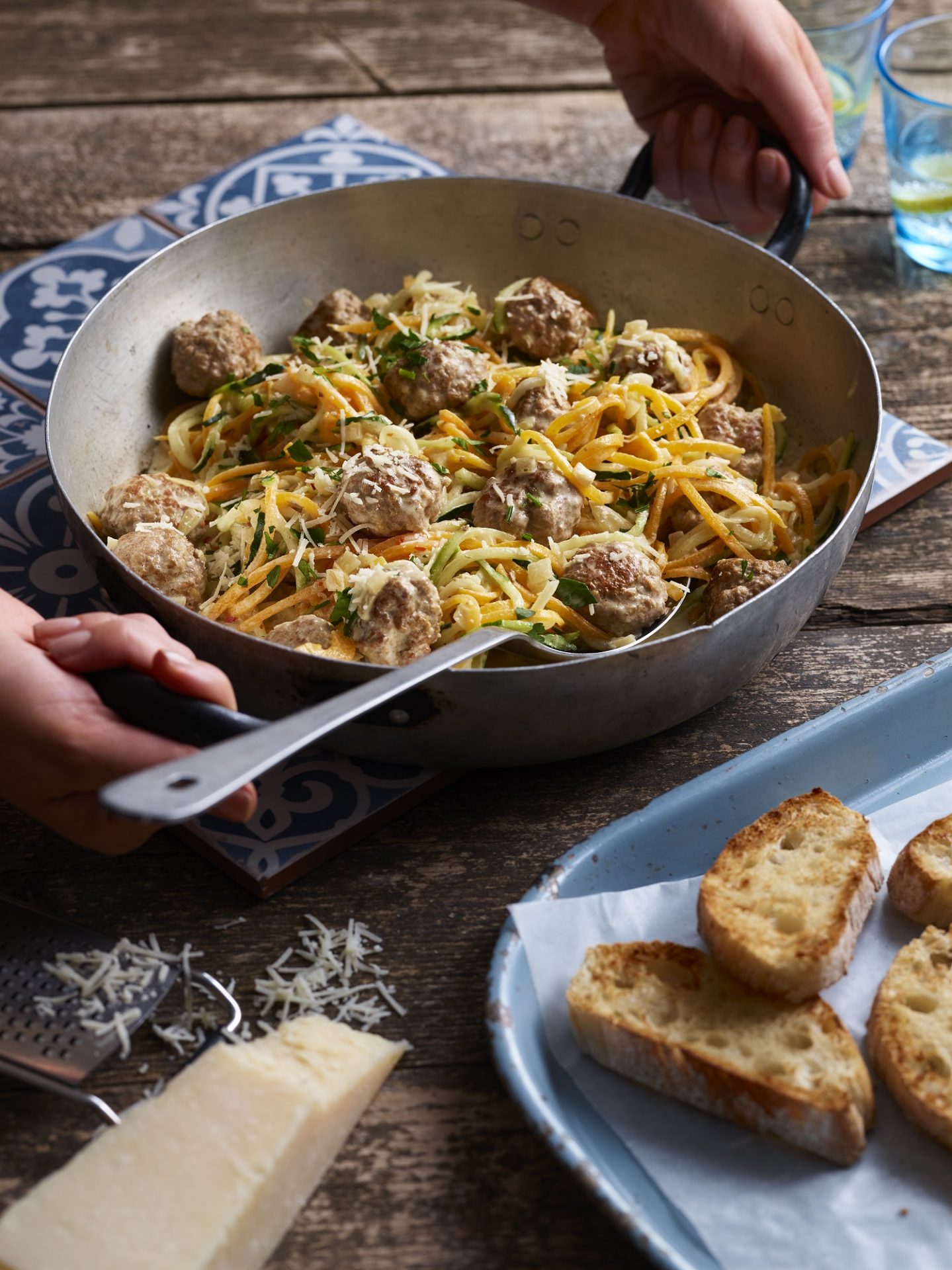 Large pan filled with meatballs and vegetable spaghetti, with large serving spoon