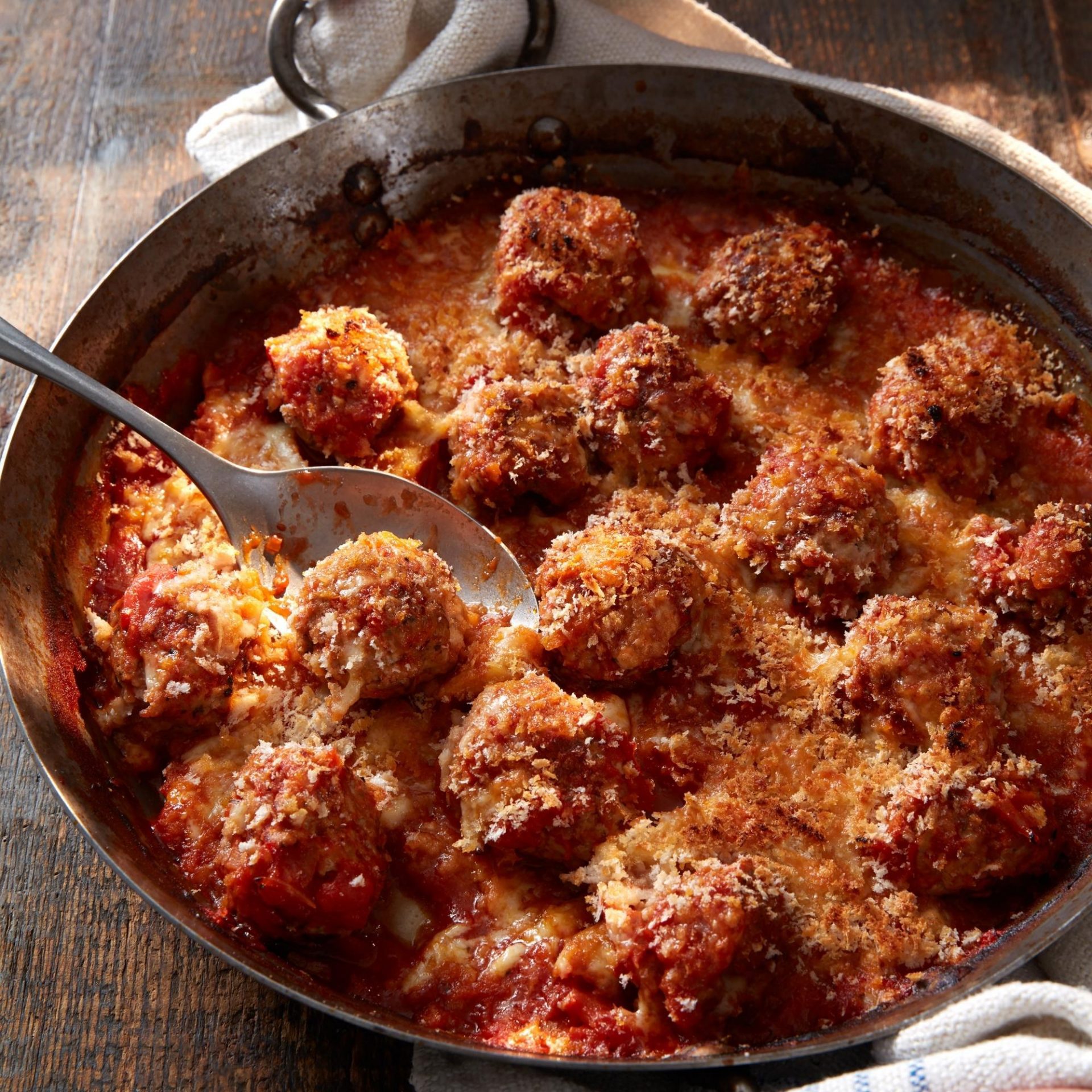 Large cast iron pan filled with pork meatballs in a red sauce, with a cheesy crumb topping