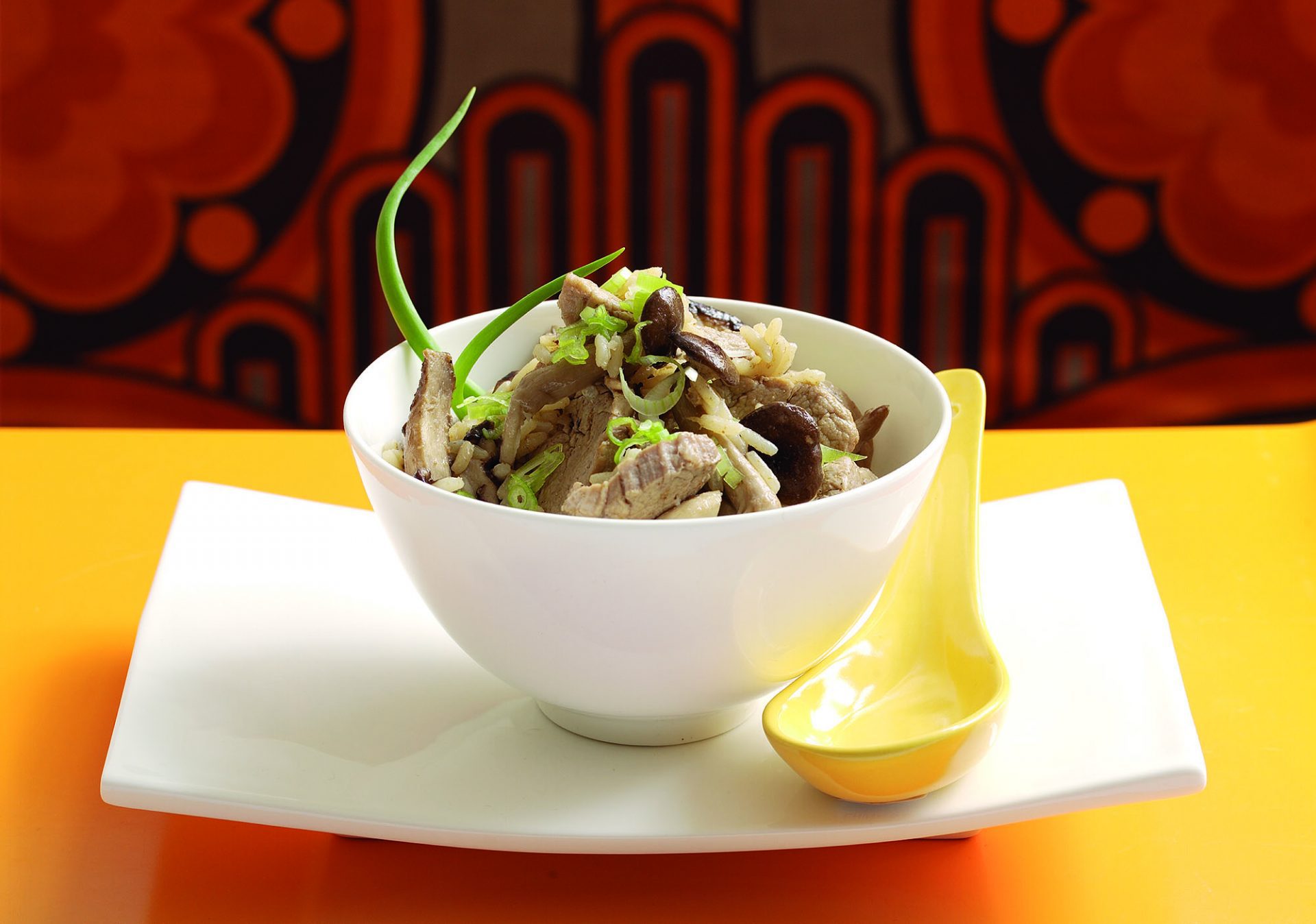 Pork pilau served in a white bowl with yellow spoon on side