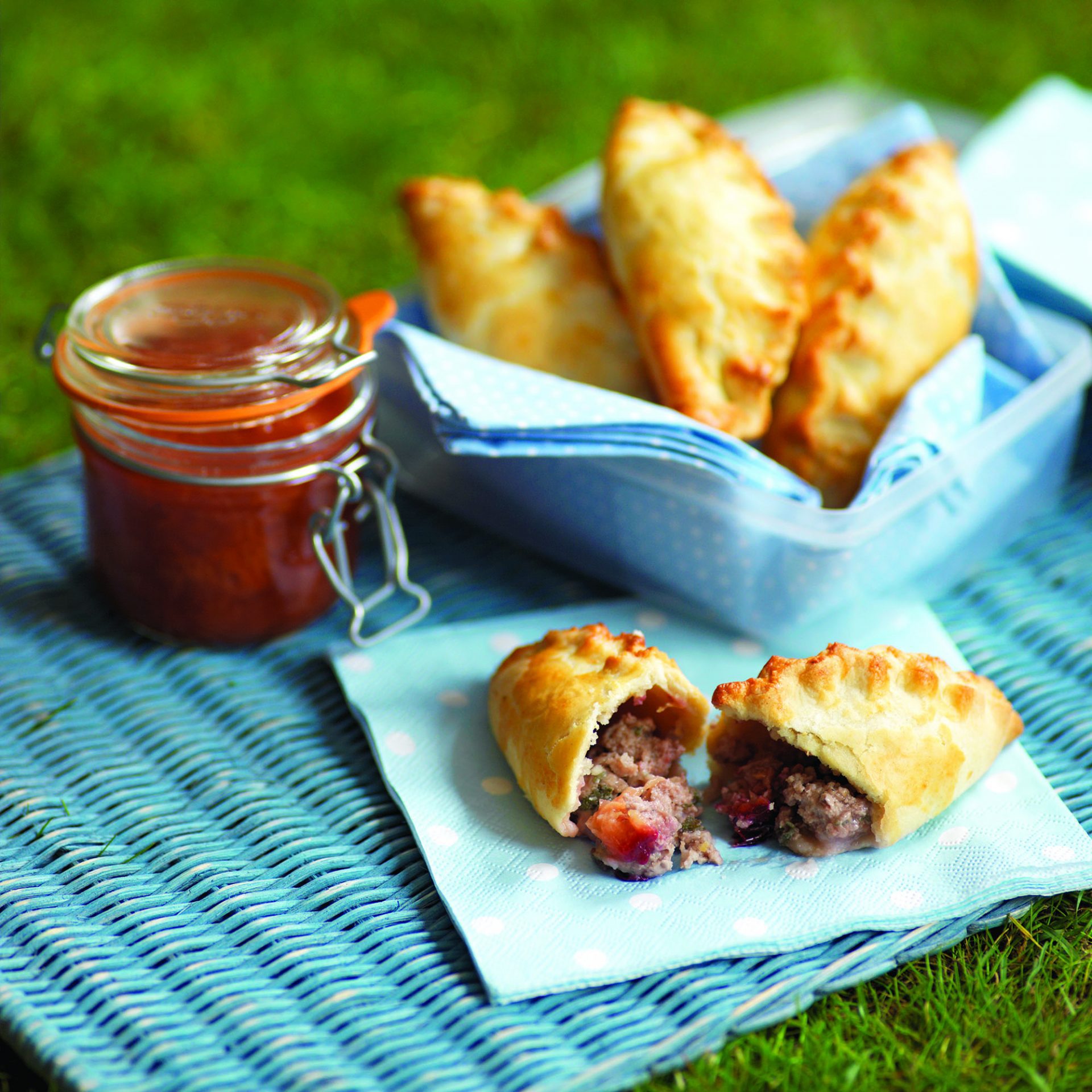 Mini pork plum and sage pasties in a container with side dip, at a picnic set up