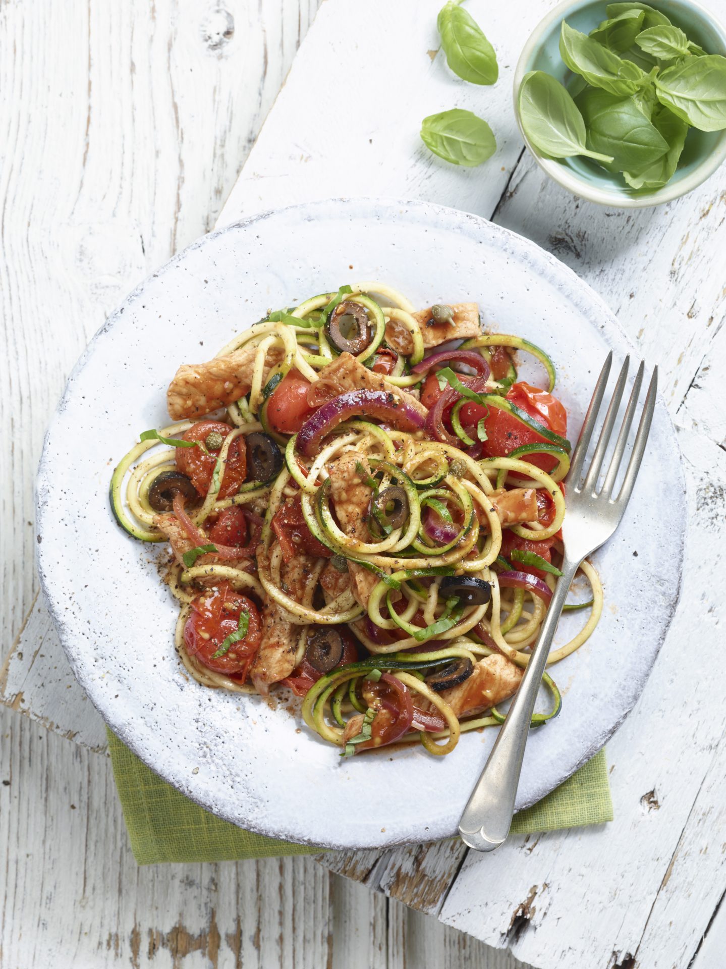 Pork puttanesca with courgetti served on a white plate with a fork